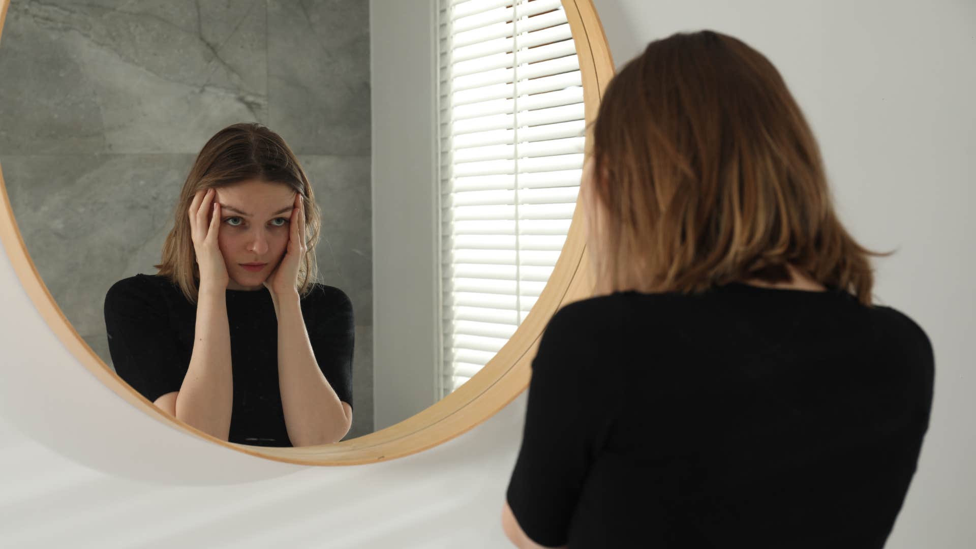woman looking in mirror criticizing herself