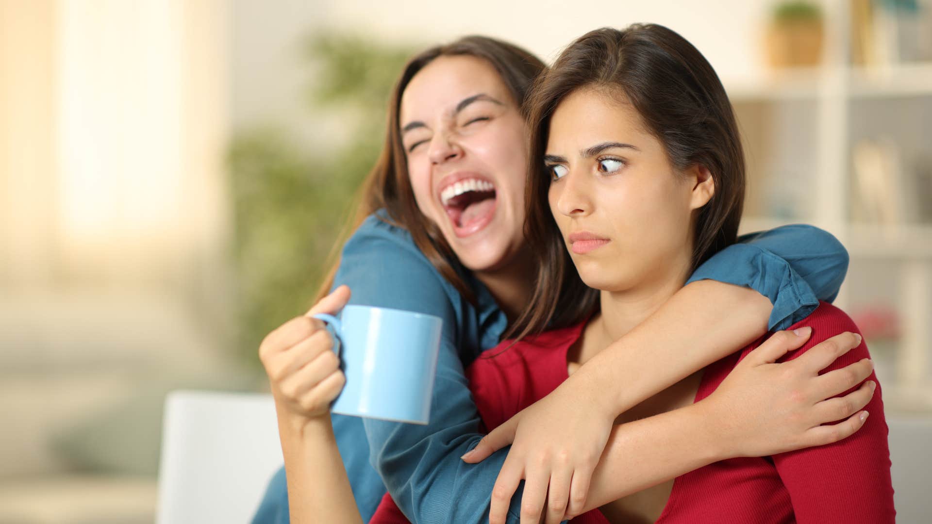 woman in red looking startled as woman in blue hugs her