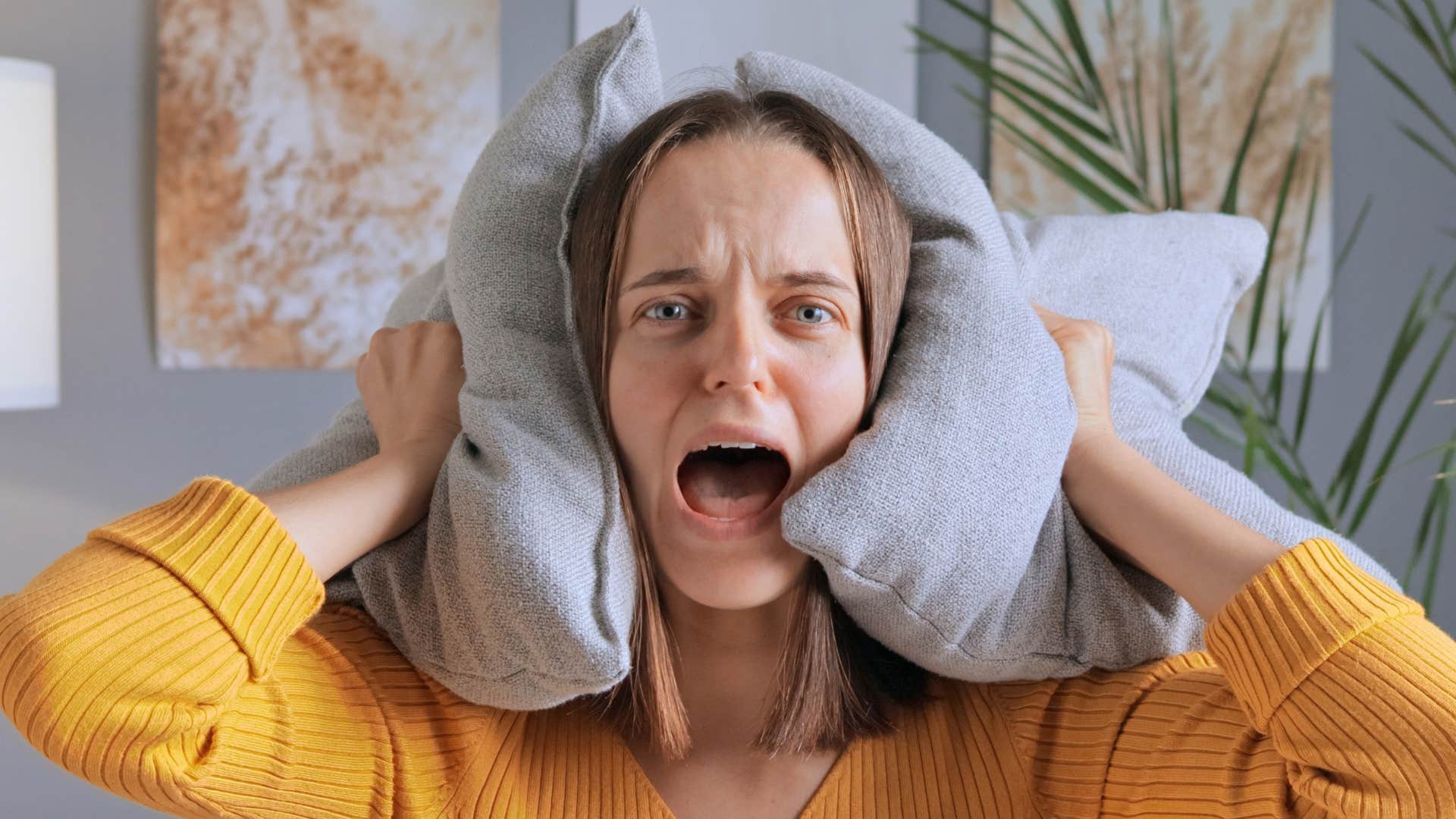 woman in orange shirt has sensory sensitivity as she covers pillow with ears