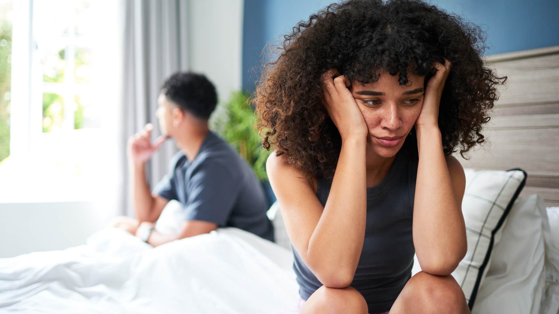 upset woman sitting on the edge of the bed away from partner