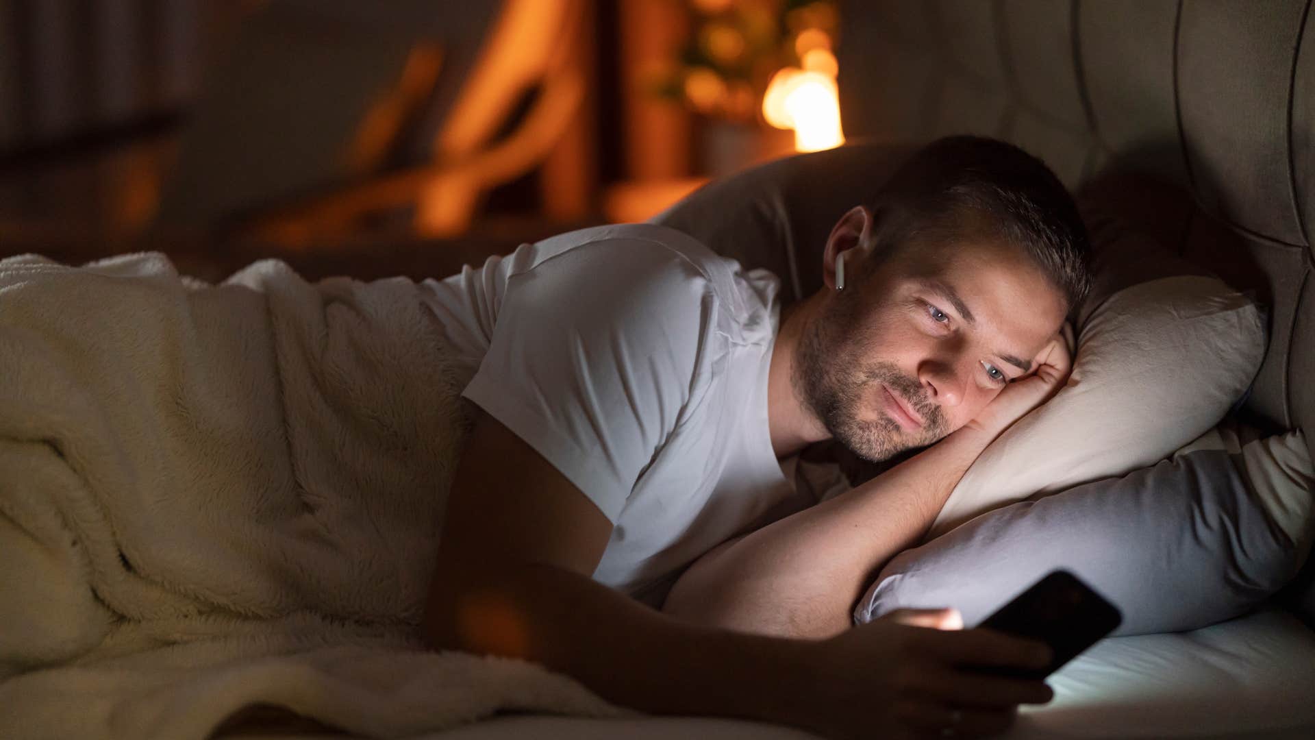 man looking at his phone while lying in bed