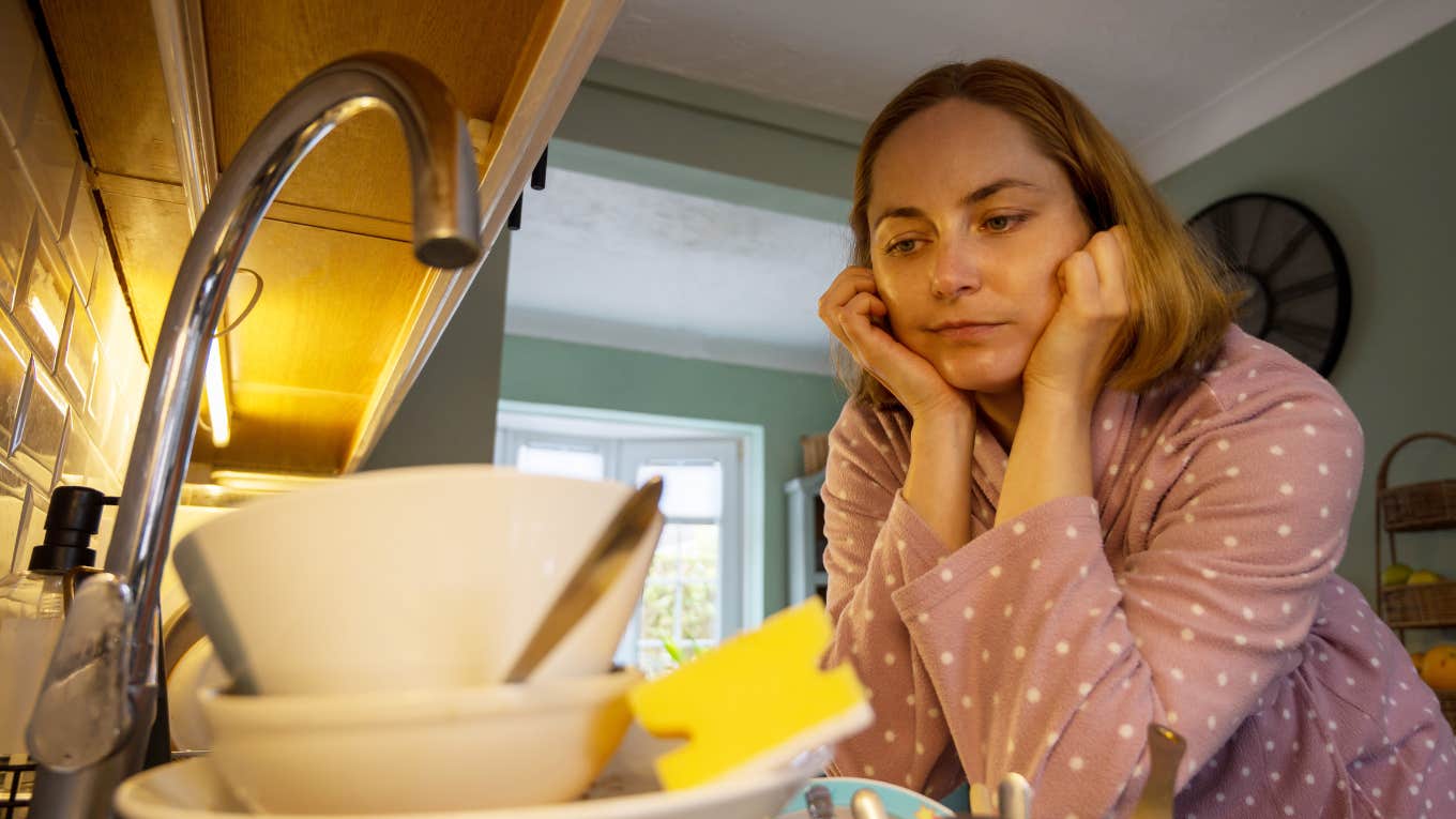 sad woman looking at dirty dishes in her sink