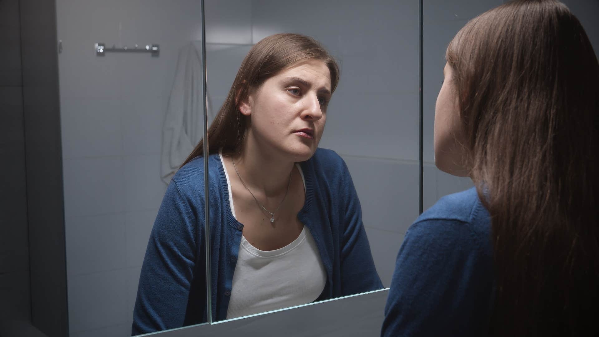 woman looking in mirror thinking