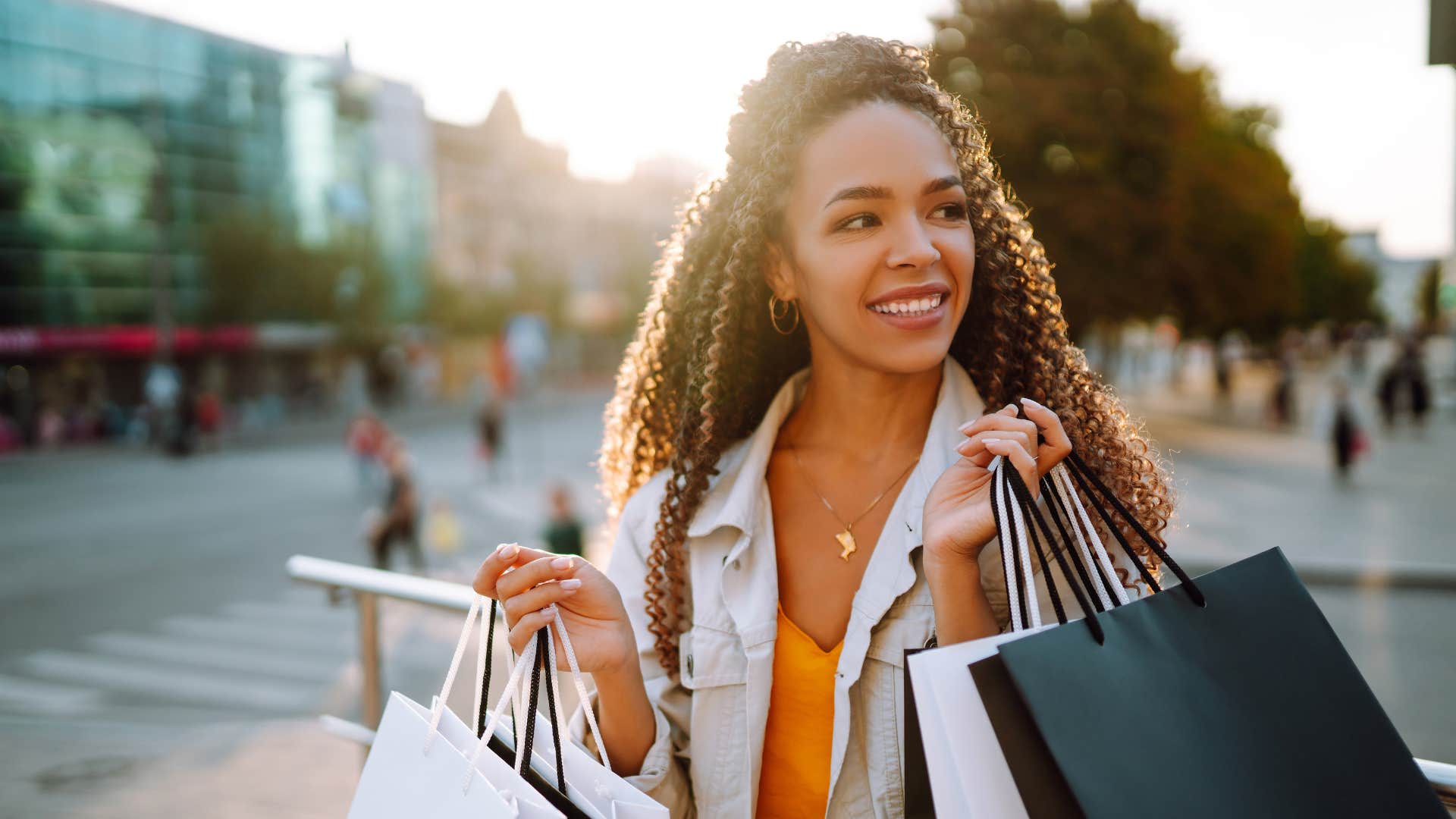 woman in white jacket having bad spending habits as she carries bags and smiles