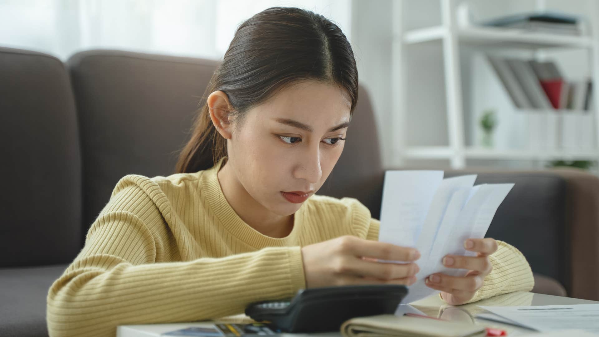 woman in yellow looking at receipts as she hates losing money by accidentally overpaying