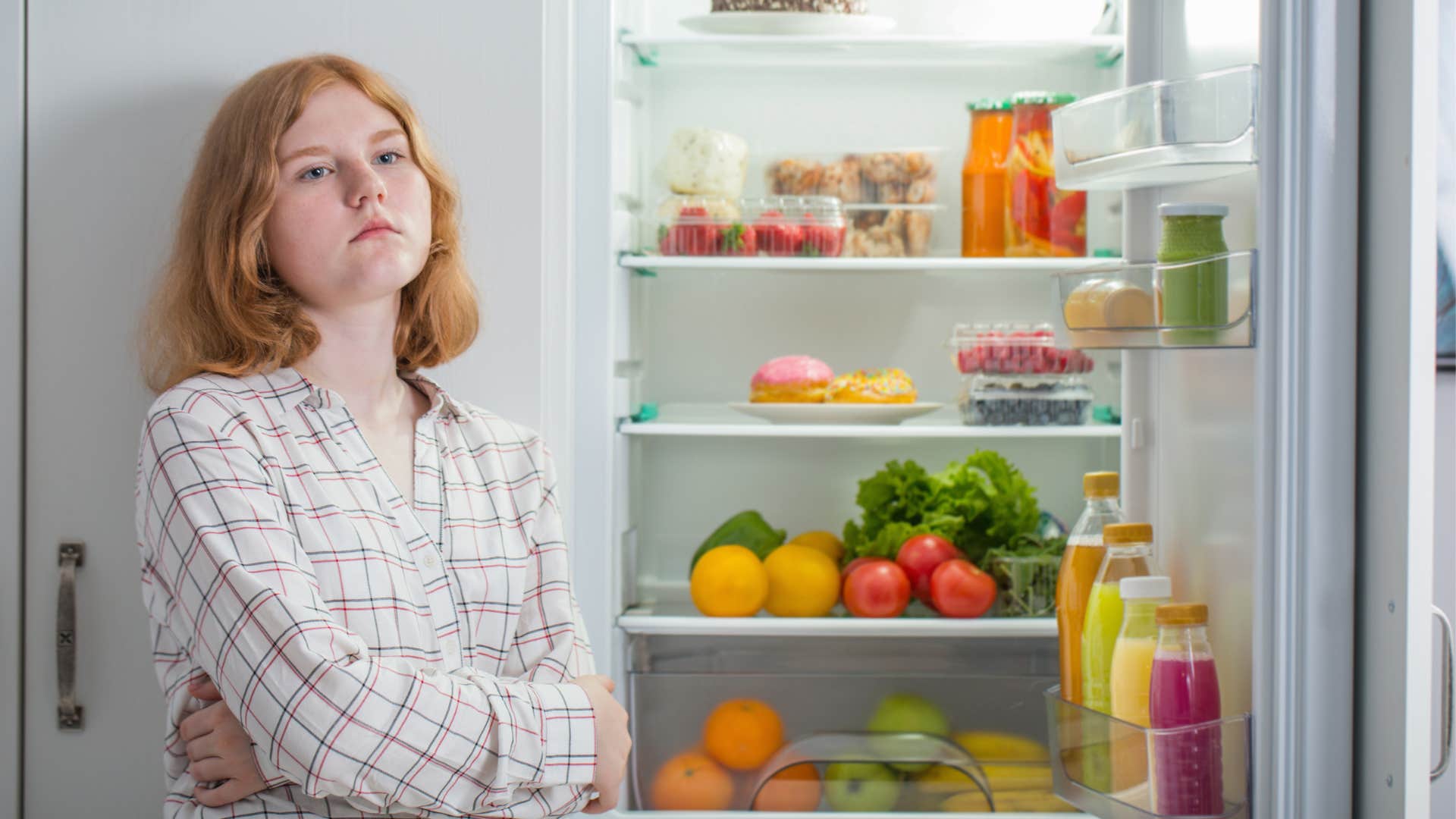 upset young woman in front of fridge refusing to eat healthy food