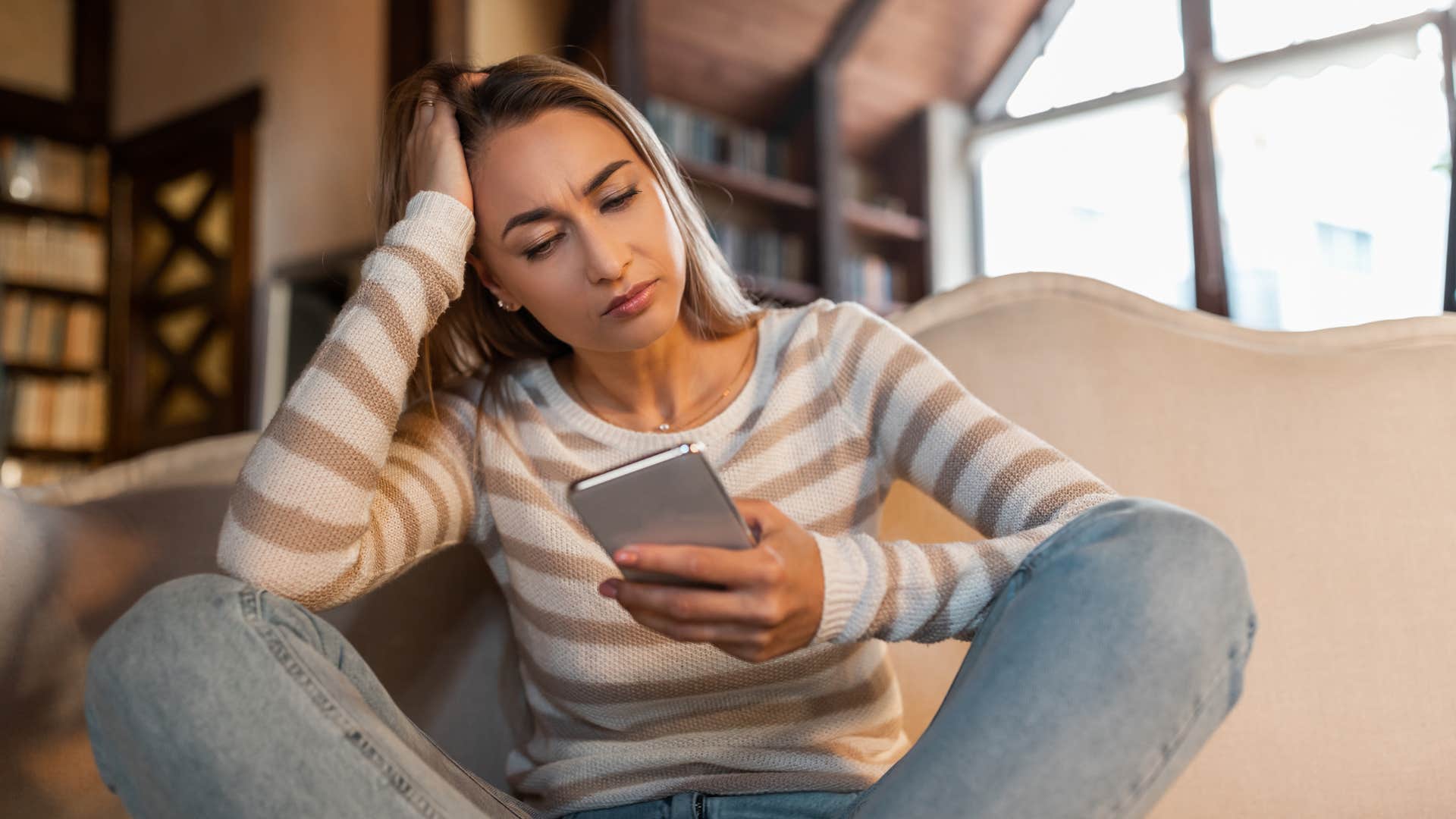 unhappy woman using her phone excessively at home