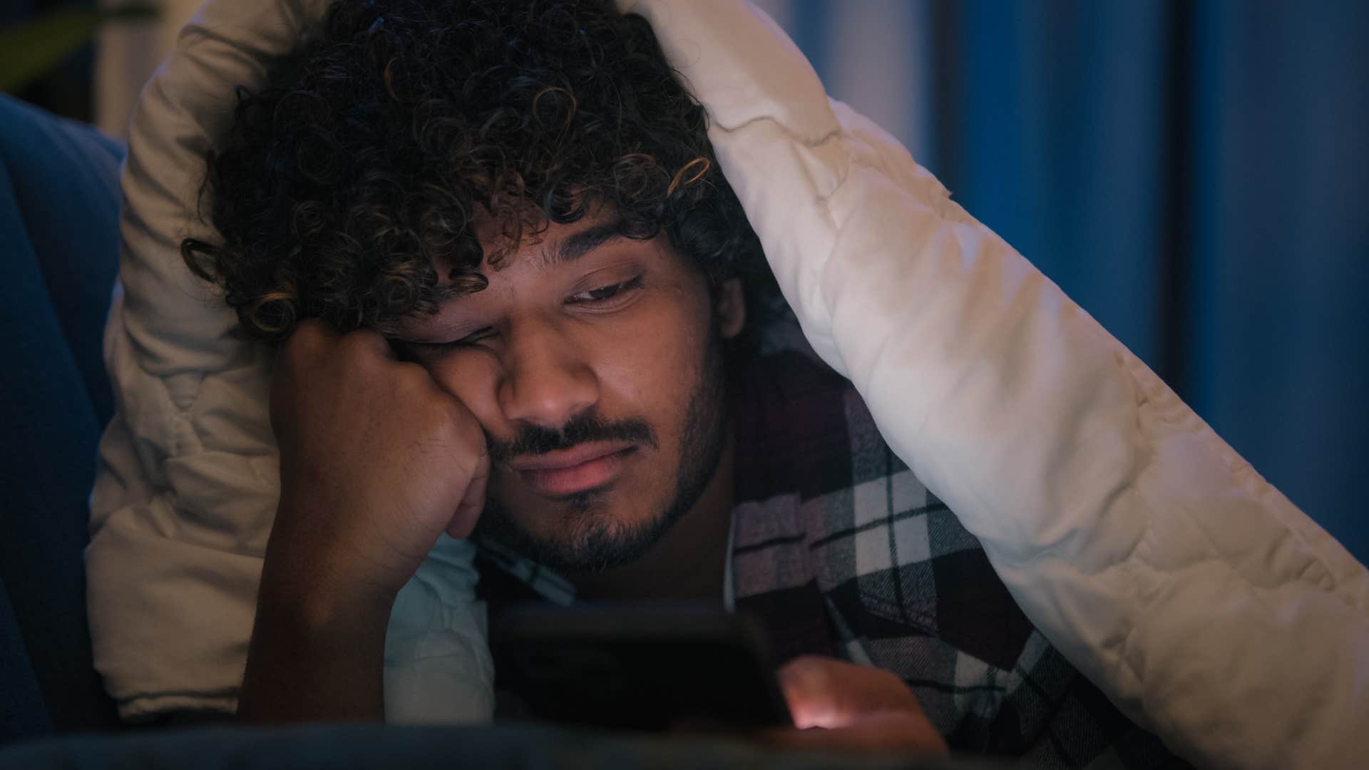 Man doomscrolling in bed on his phone.