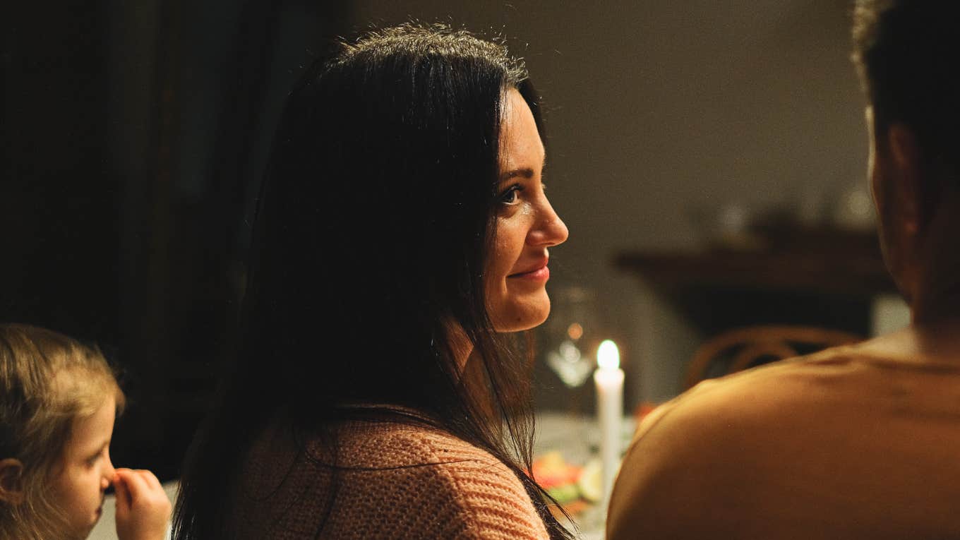 Woman looking knowingly at partner while family is gathered around a Thanksgiving table showing how certain phrases can instantly change the holiday vibe.