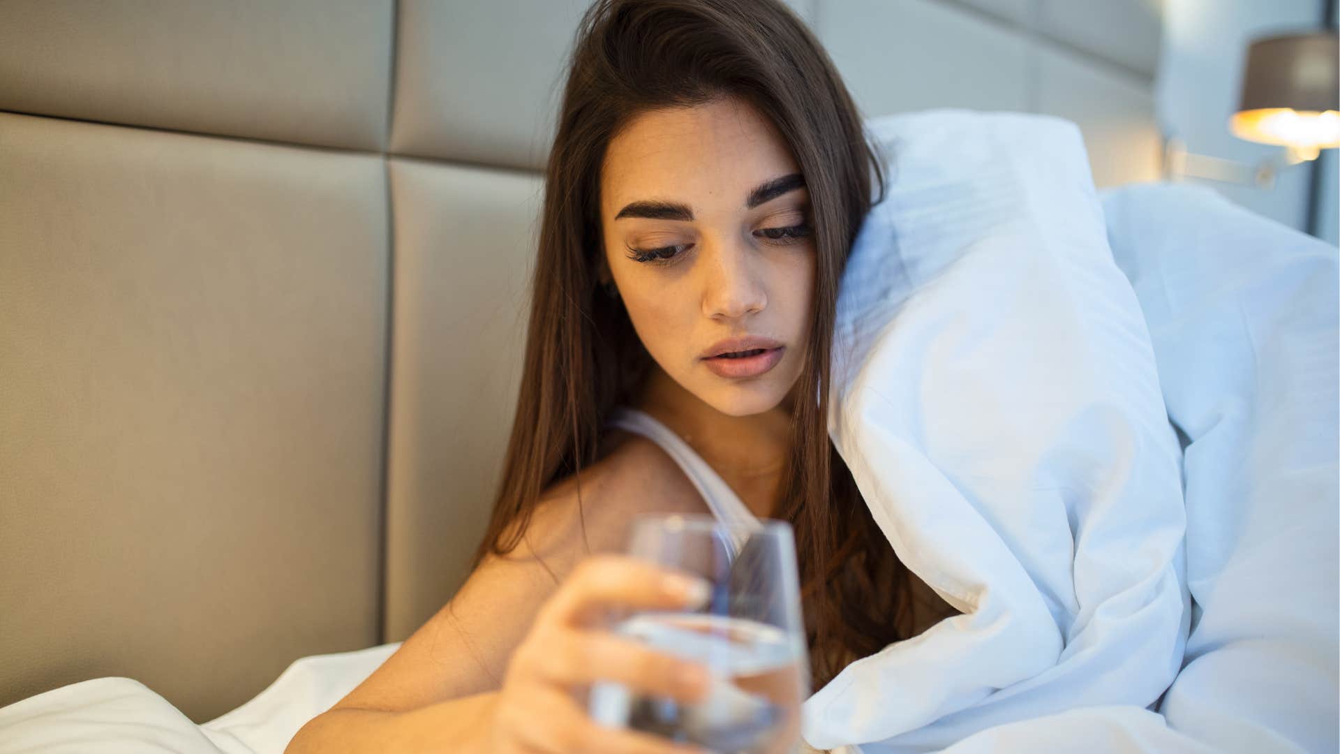 woman in bed staying hydrated drinking water