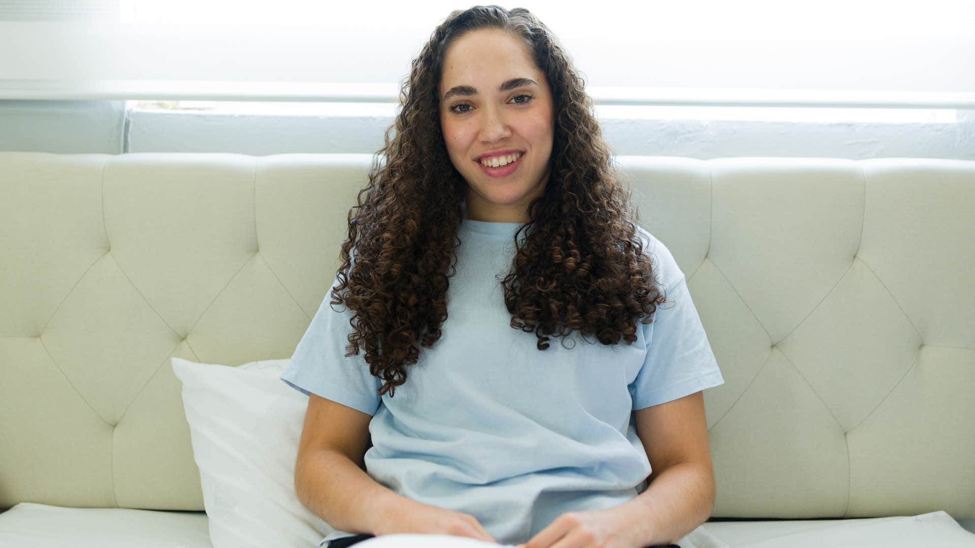 woman sitting in her clean bedroom smiling