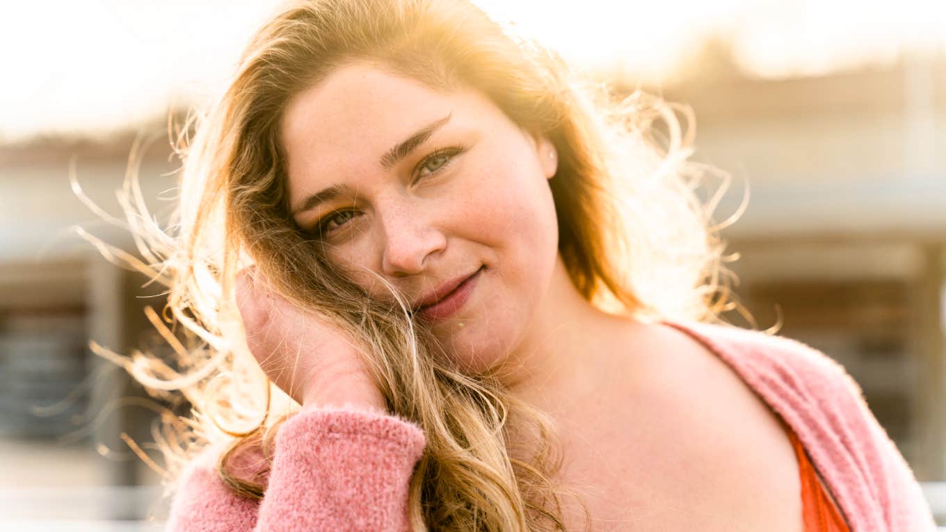 Confident woman smiling softly in warm sunlight showing the art of self-worth and the habits of people who don’t need anyone to confirm their greatness.