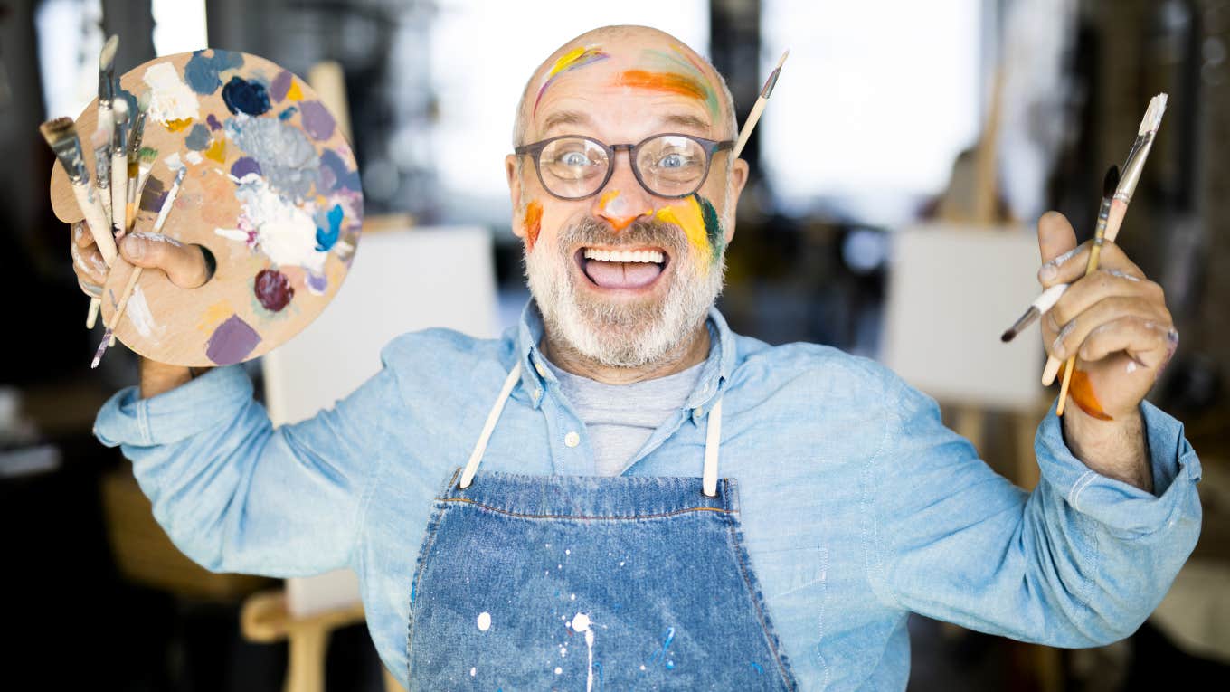 Ecstatic mature artist holding a palette and paintbrushes showing the art of starting over and the wild choices that completely rewrite your life.