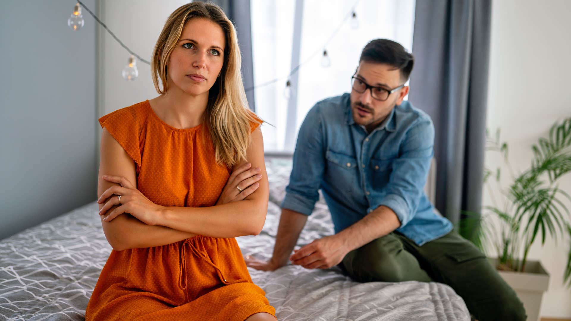 upset woman sitting on edge of bed away from partner