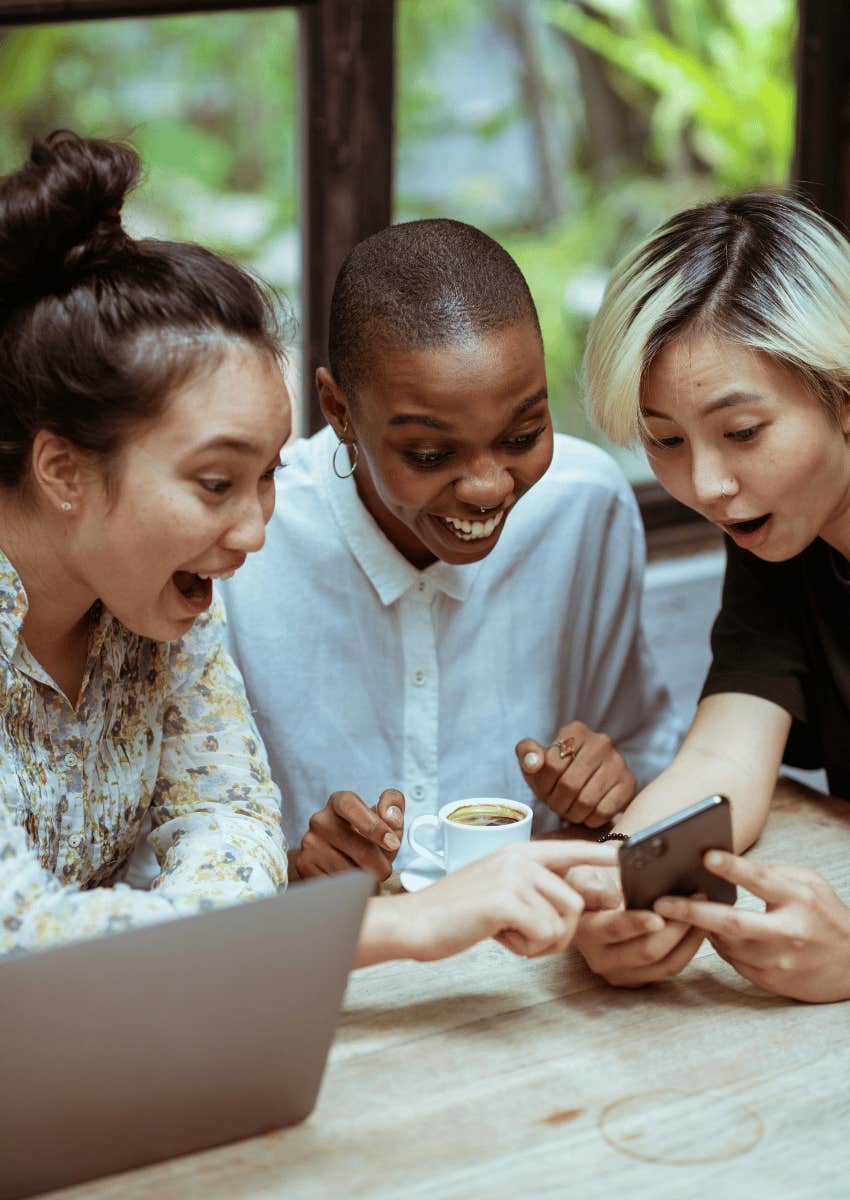 group of women looking down at phone with shock and smiling