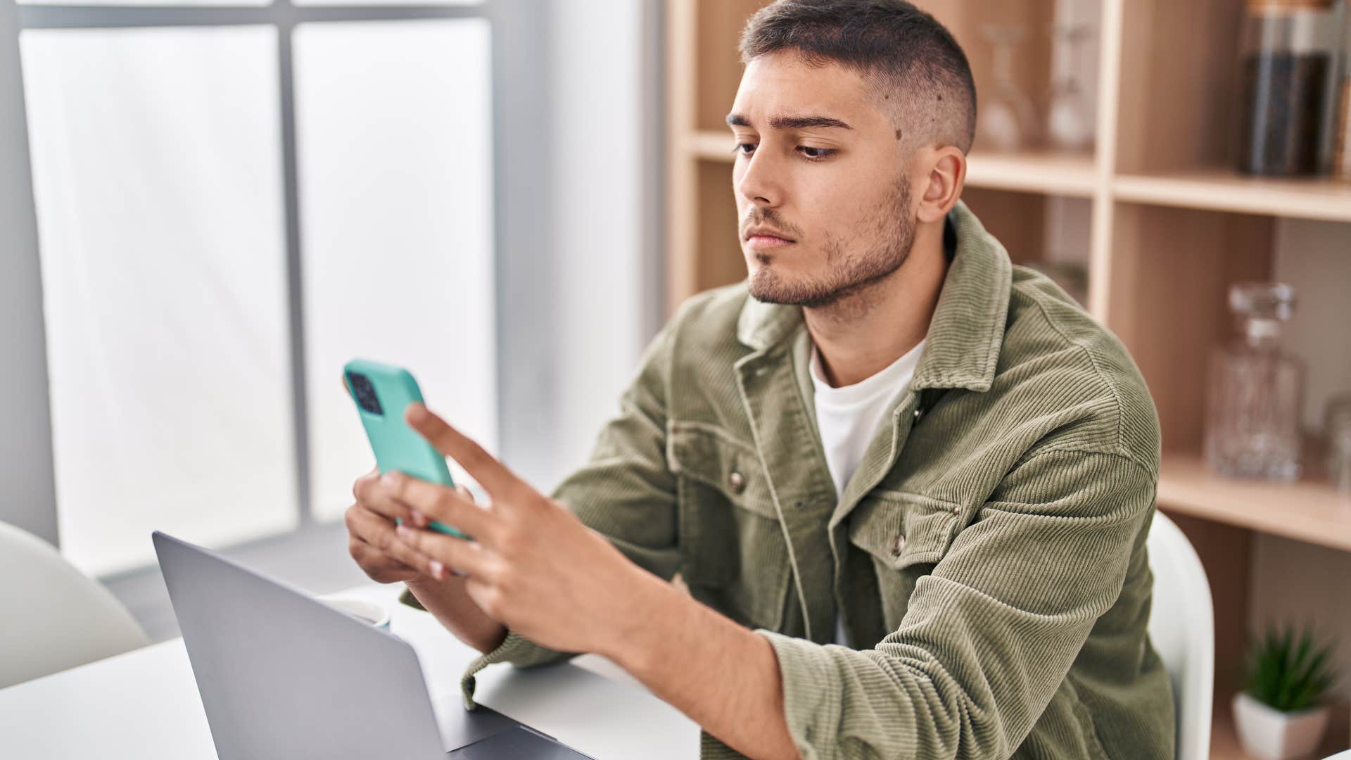 man sitting in front of laptop texting on his phone
