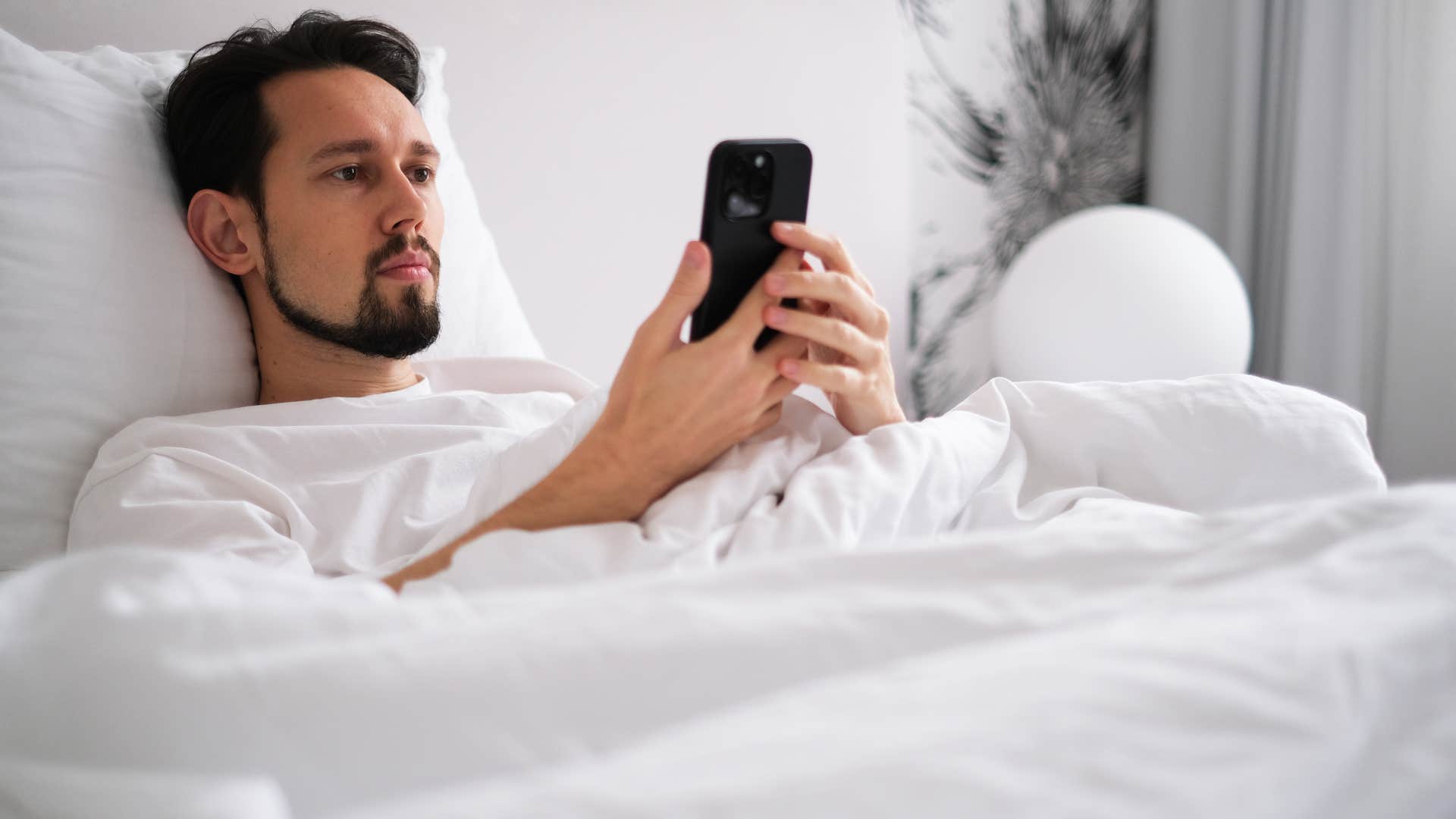 man lying in bed looking at his phone