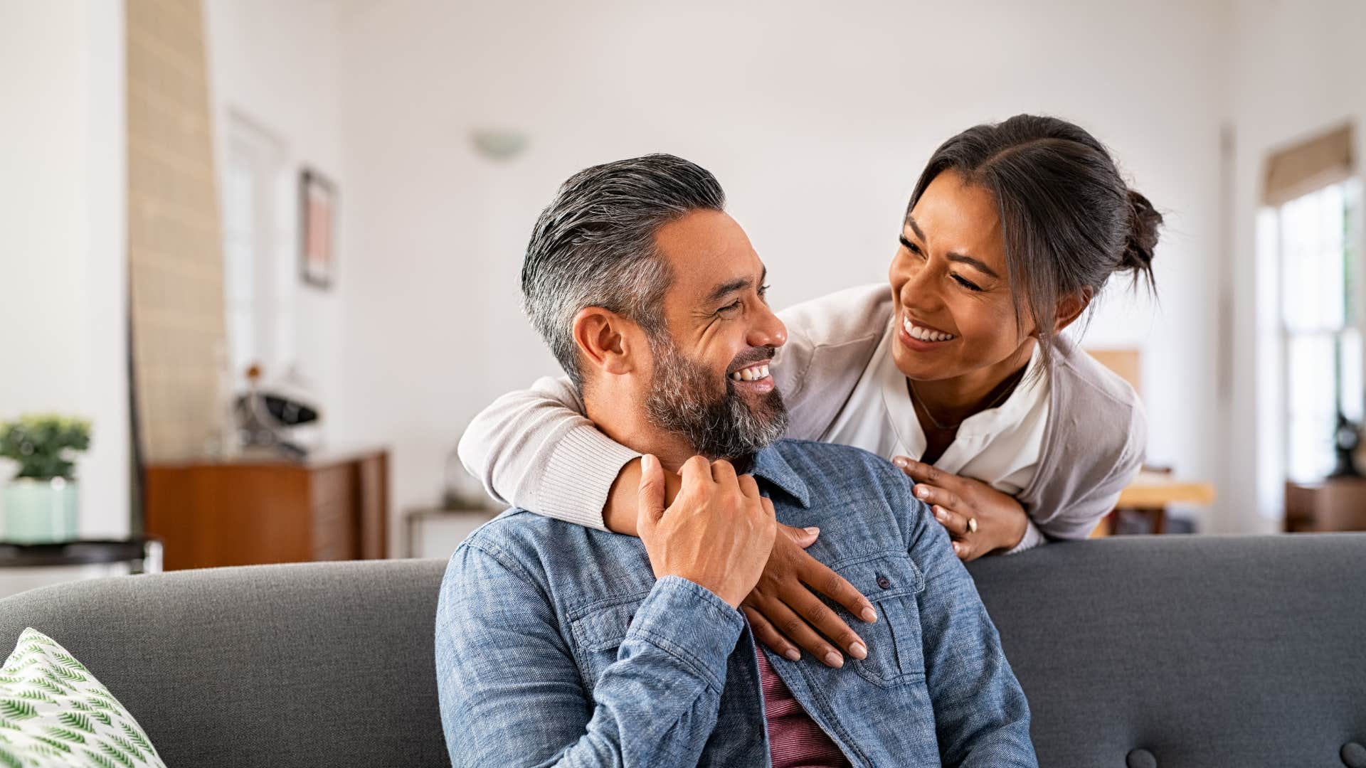 wife hugging husband sitting on couch