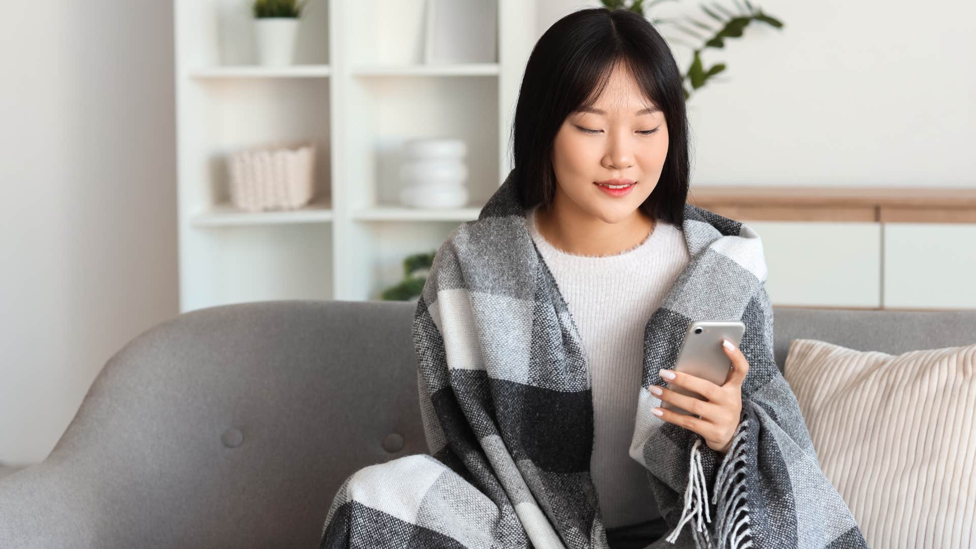 woman sitting on couch wrapped up in blanket feeling cozy