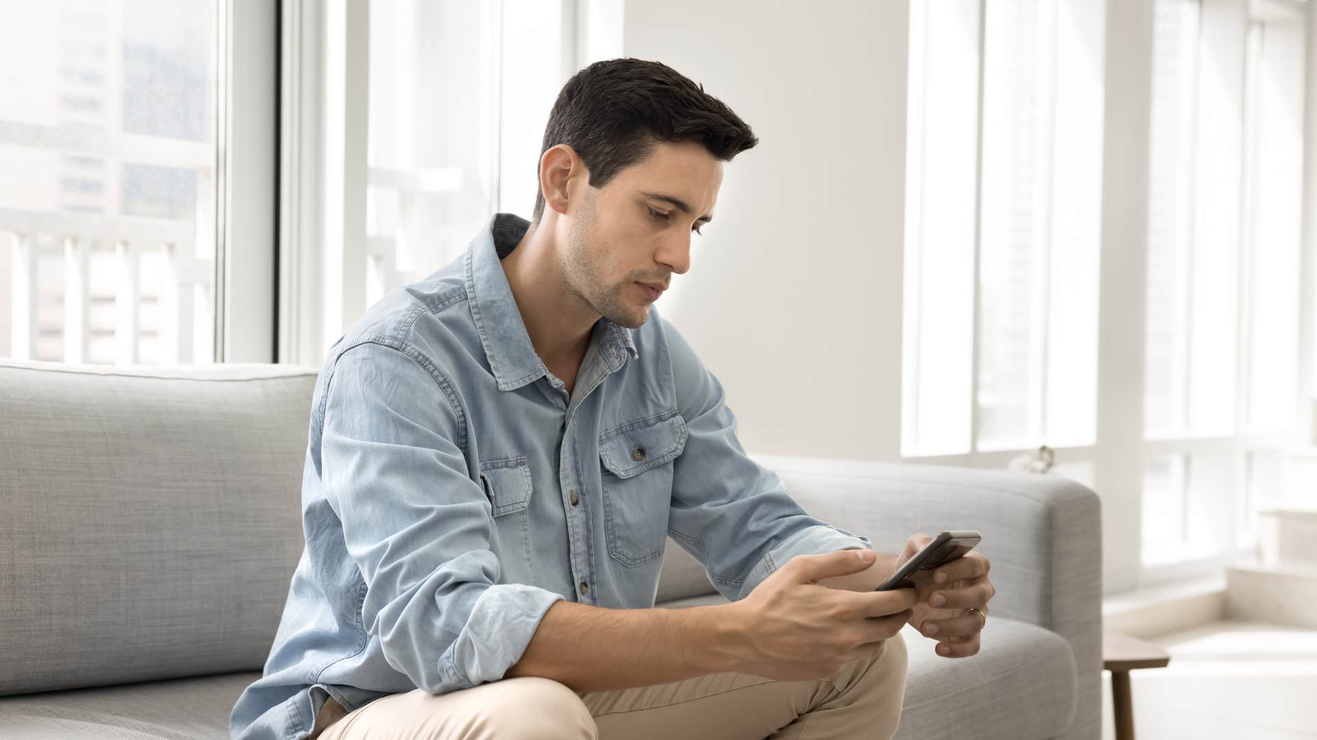 lonely man sitting on couch looking at his phone