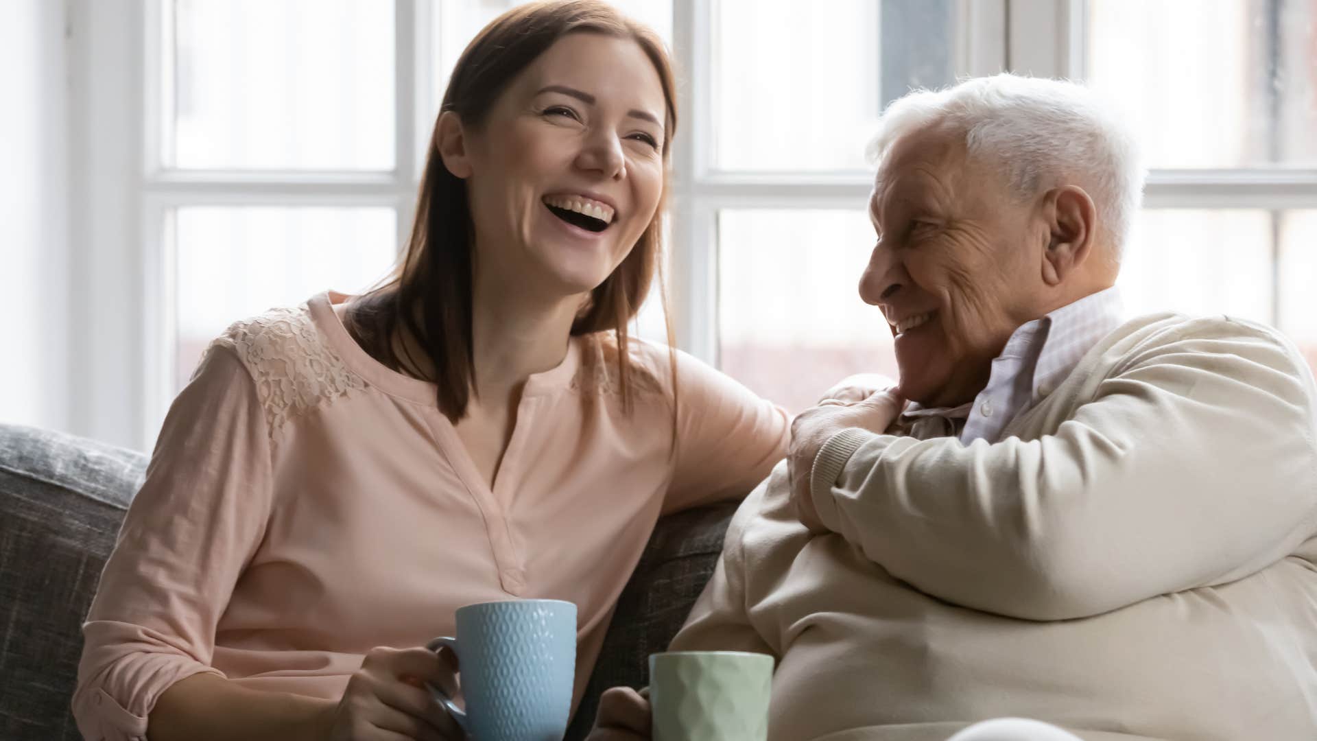 older father laughing with adult daughter on couch