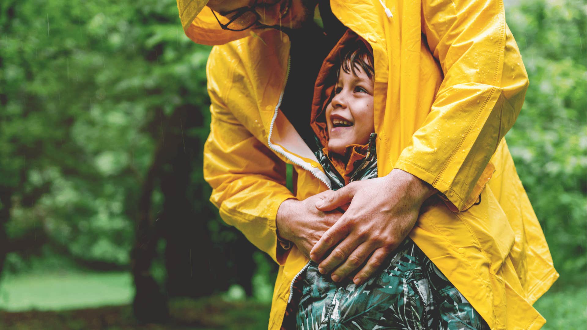 father protecting young son with raincoat