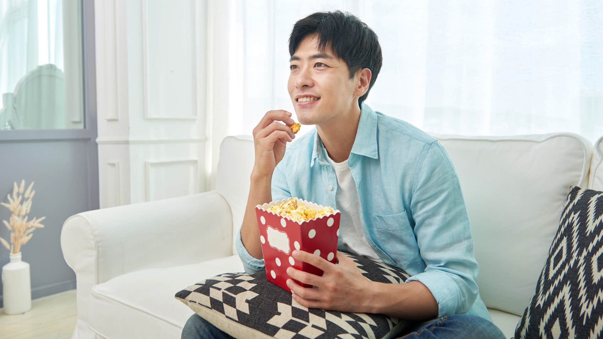 man in blue shirt sitting on couch eating comfort snacks