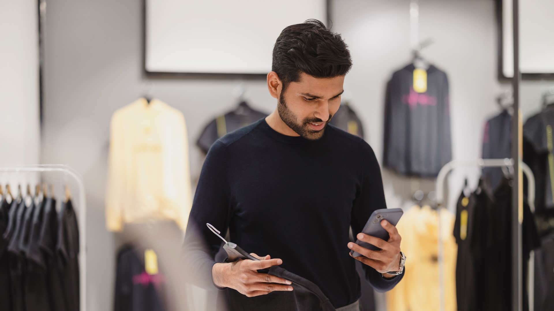 man in black shirt on phone as he tries on new clothing and shoes