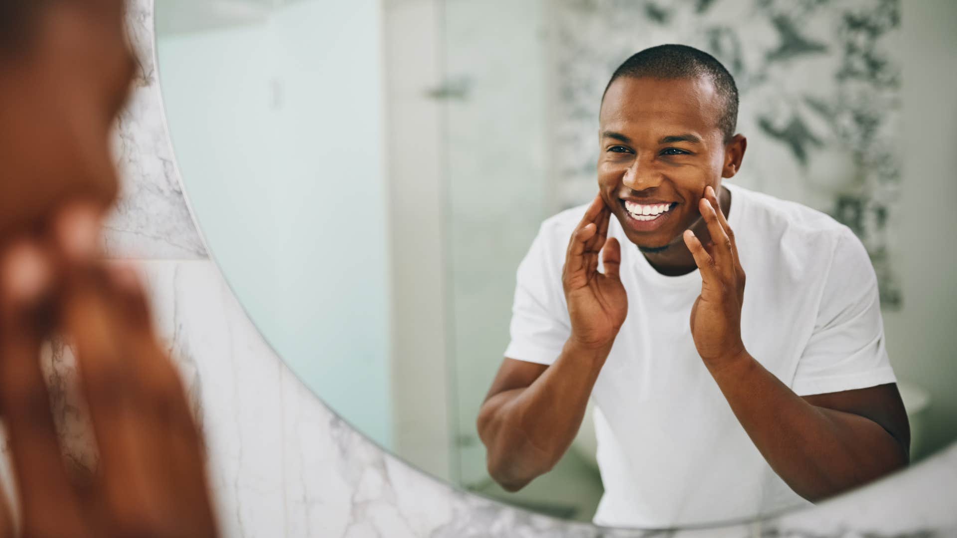 man in white shirt applying personal care products in mirror as he smiles