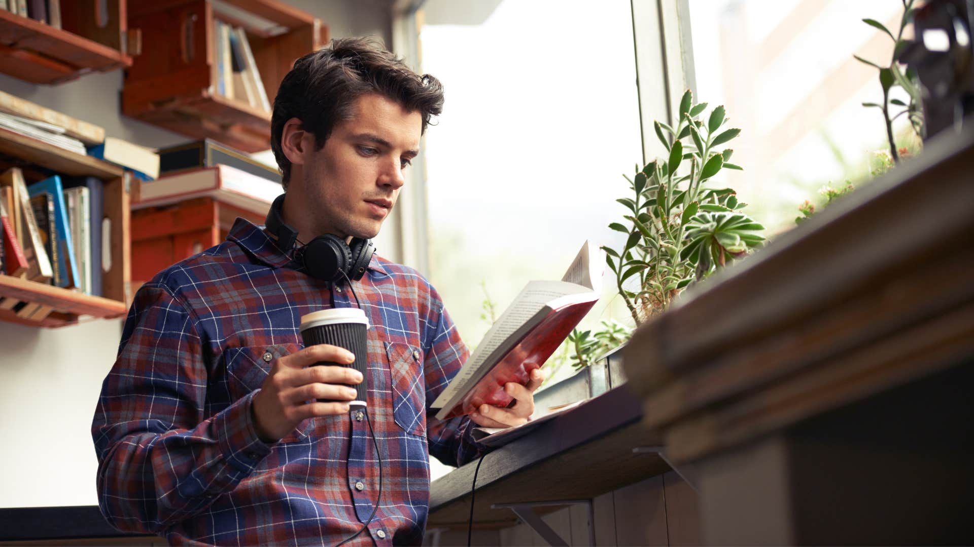 man in plaid shirt reading self help book as he drinks coffee