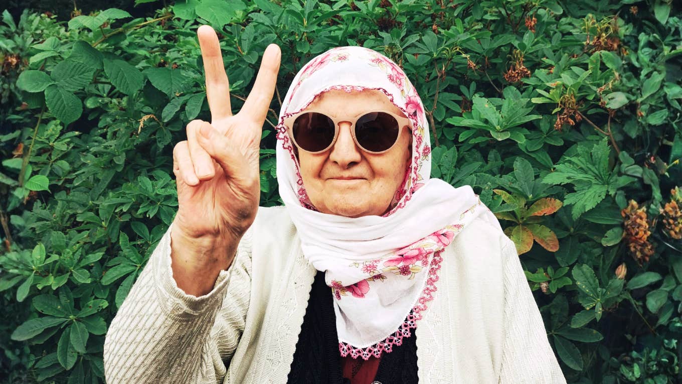 seventy-two-year-old mother wearing sunglasses and a floral scarf flashing a playful peace sign, capturing the bold moment she quit bacon and her forty-year marriage on the same day