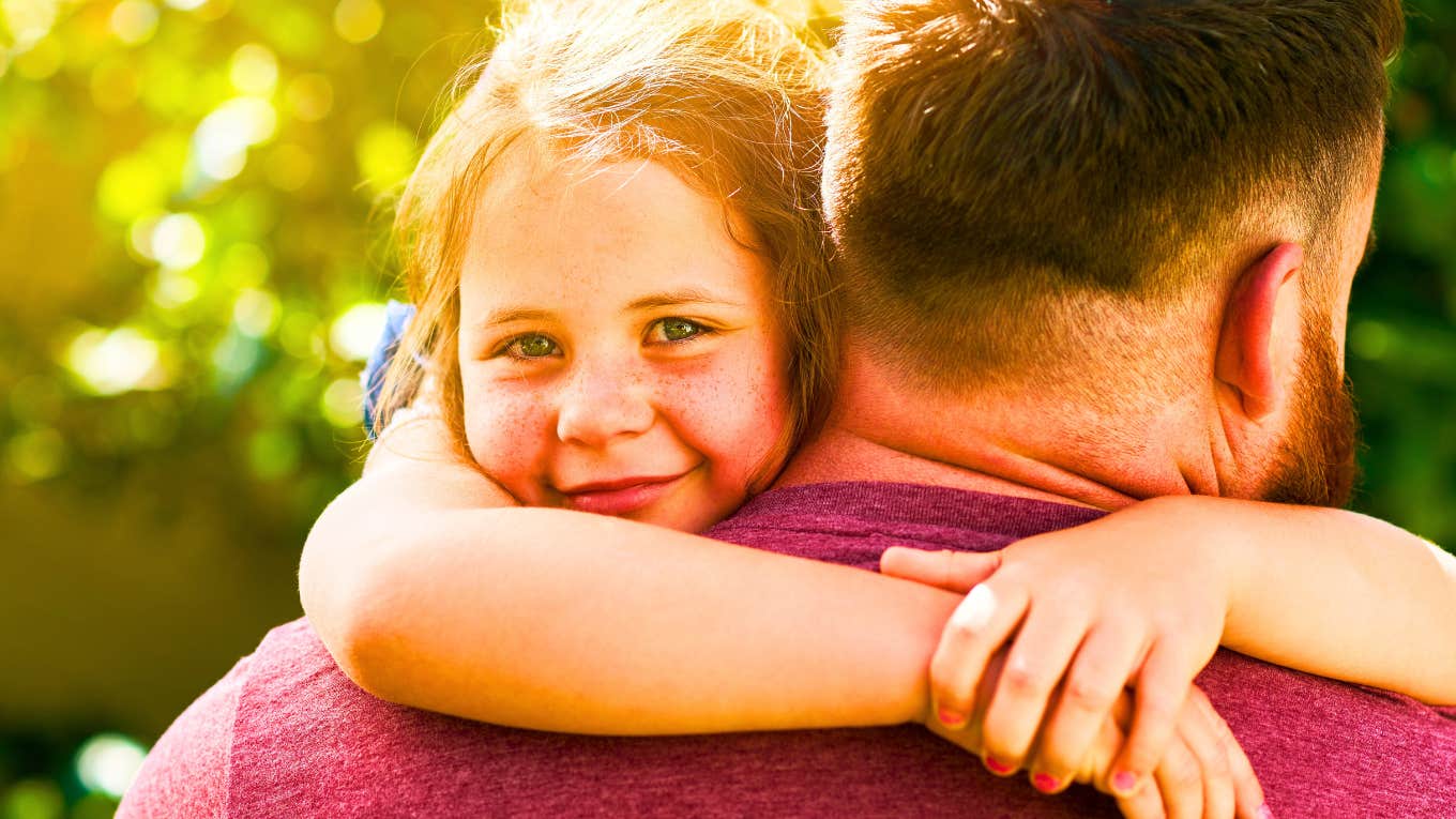 Smiling child hugging an adult’s shoulders outdoors, representing an article about parenting habits that raise genuinely good humans