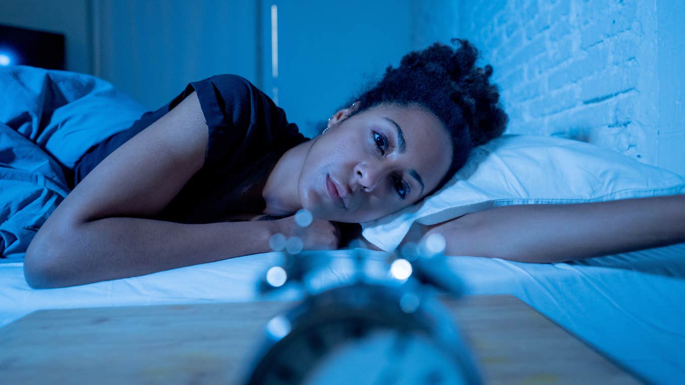 tired woman looking at clock as she stays up late