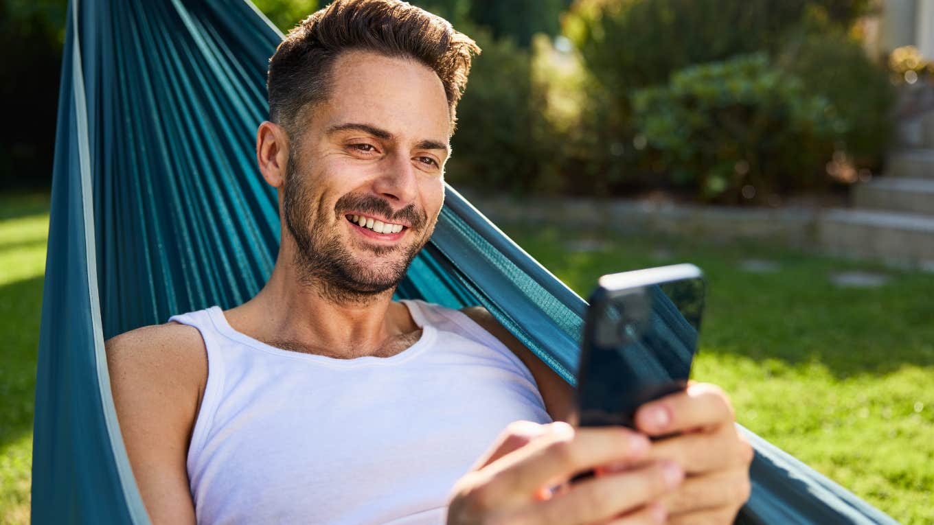 smiling man in hammock looking at his phone