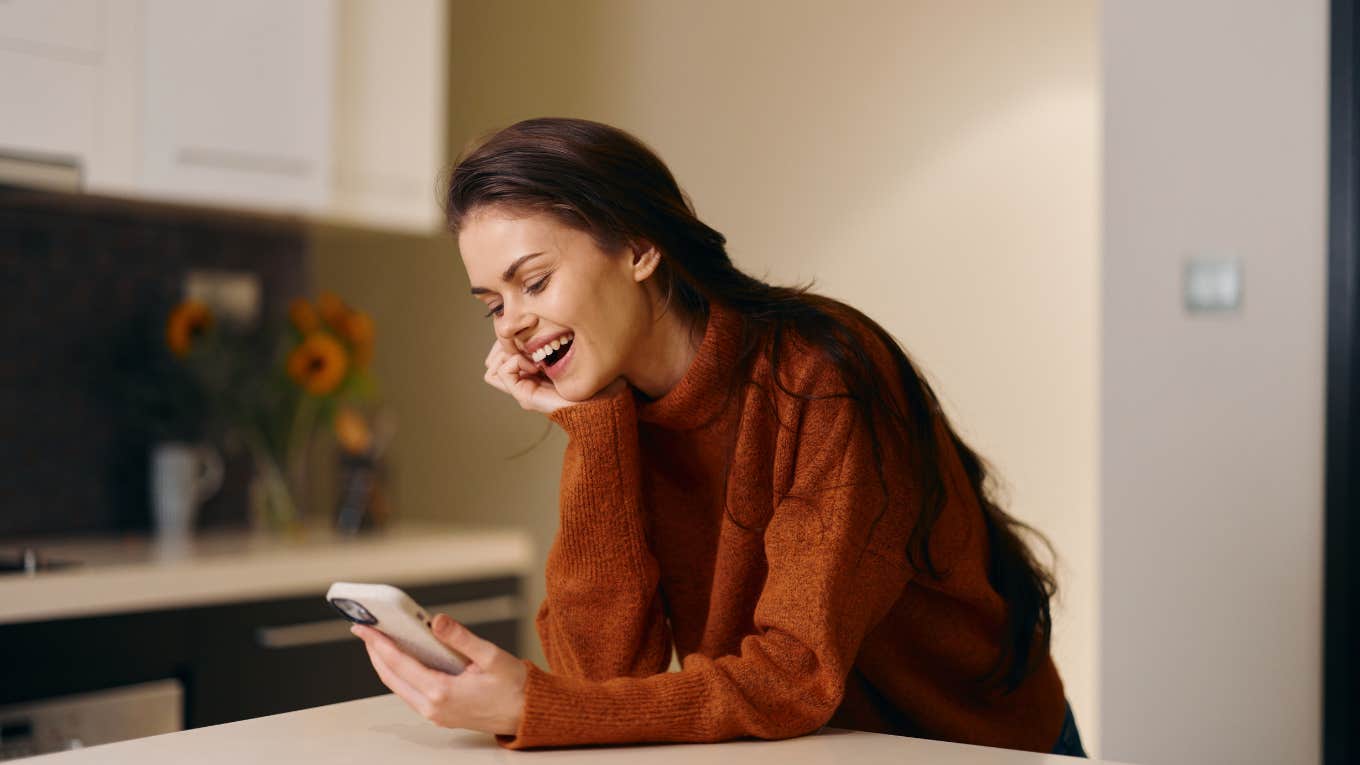 woman at home leaning on counter looking at phone