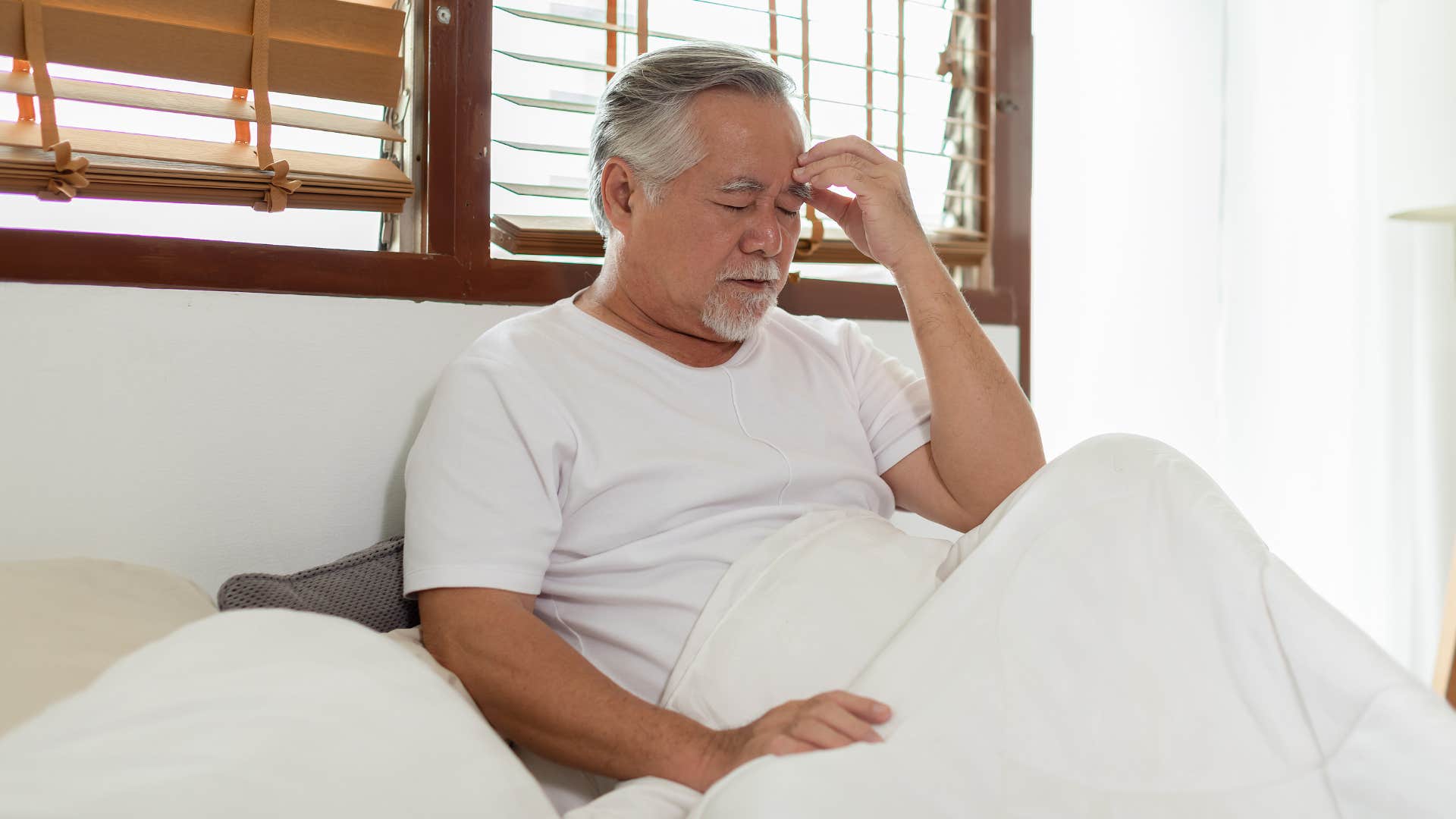 man sitting in bed with morning aches and pains