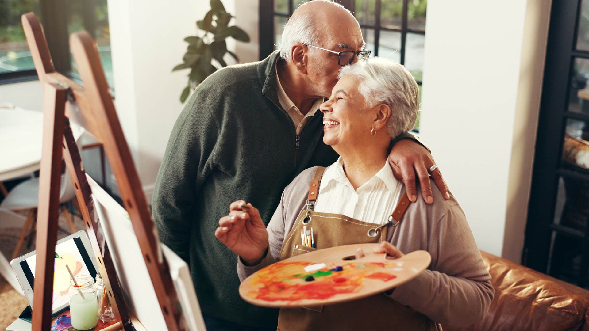 intelligent woman painting at home while husband kisses her head