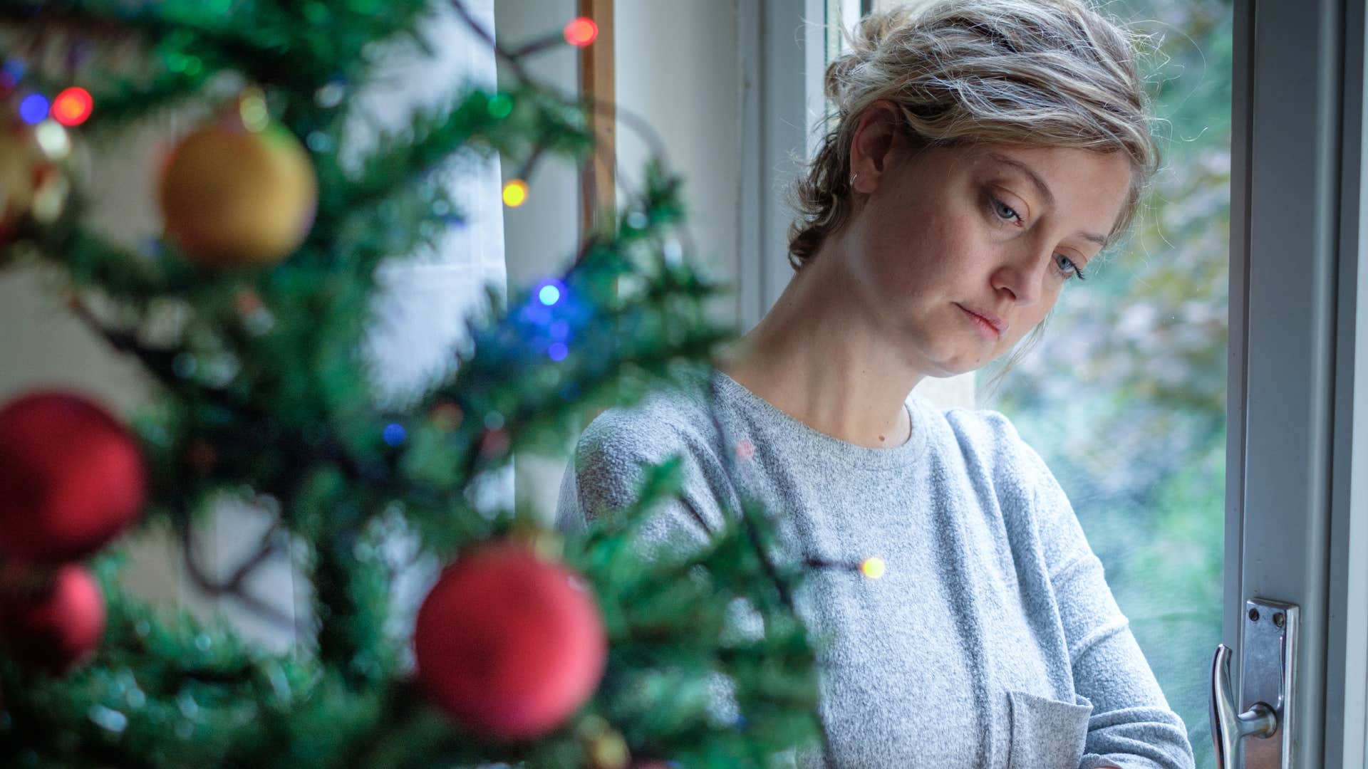 sad woman standing next to christmas tree at home