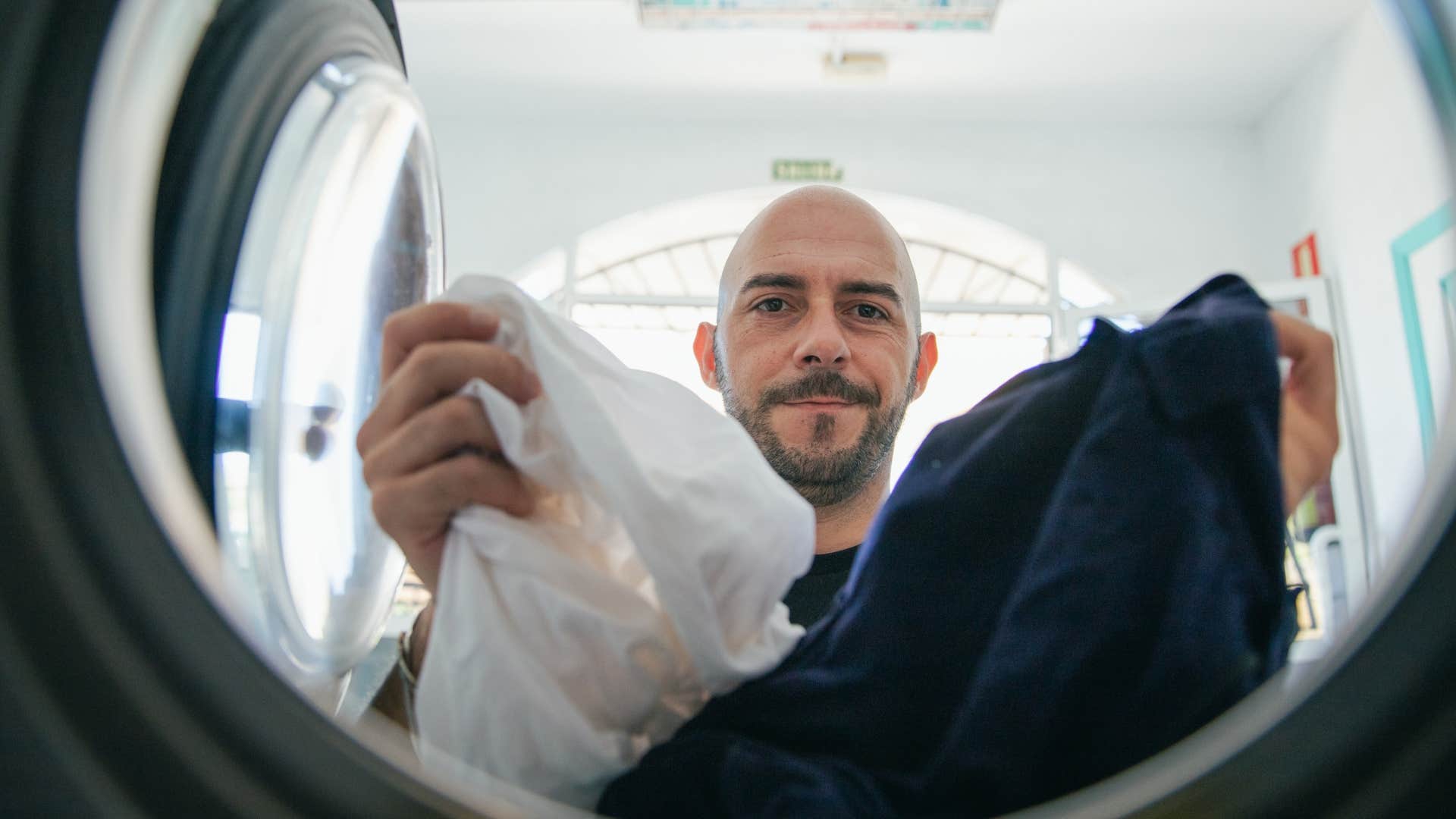 man putting his bedsheets in the washing machine