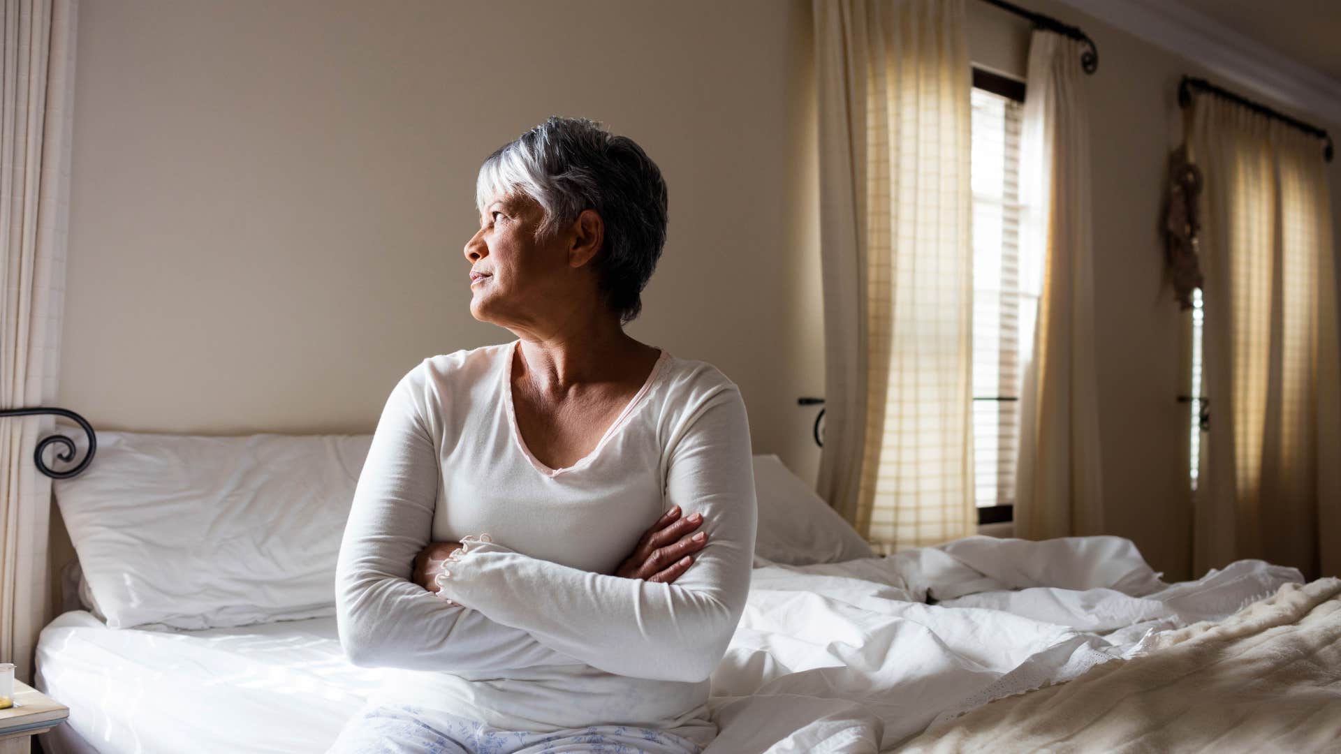sad older woman sitting on unmade bed