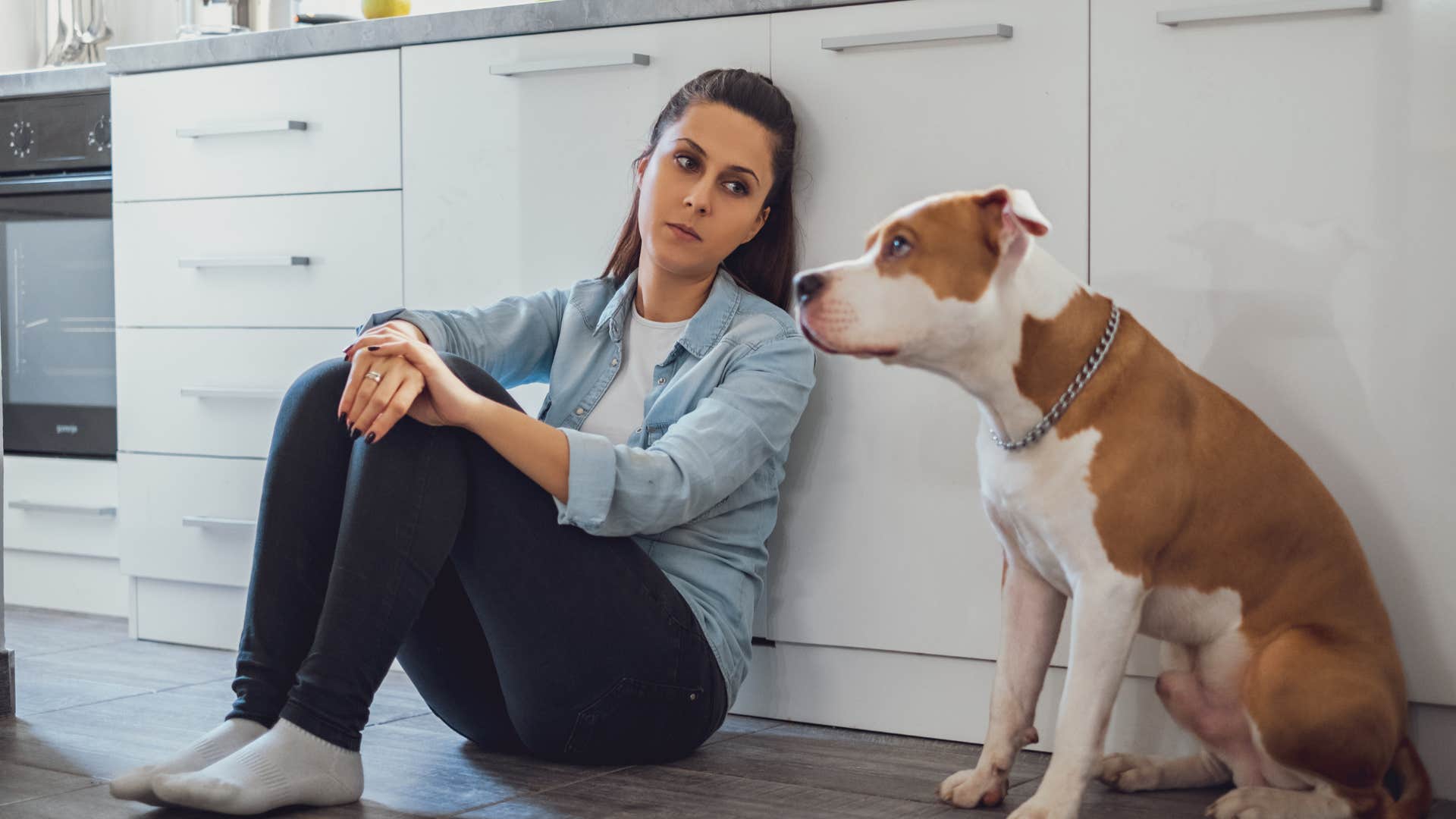 sad woman sitting with dog on kitchen floor