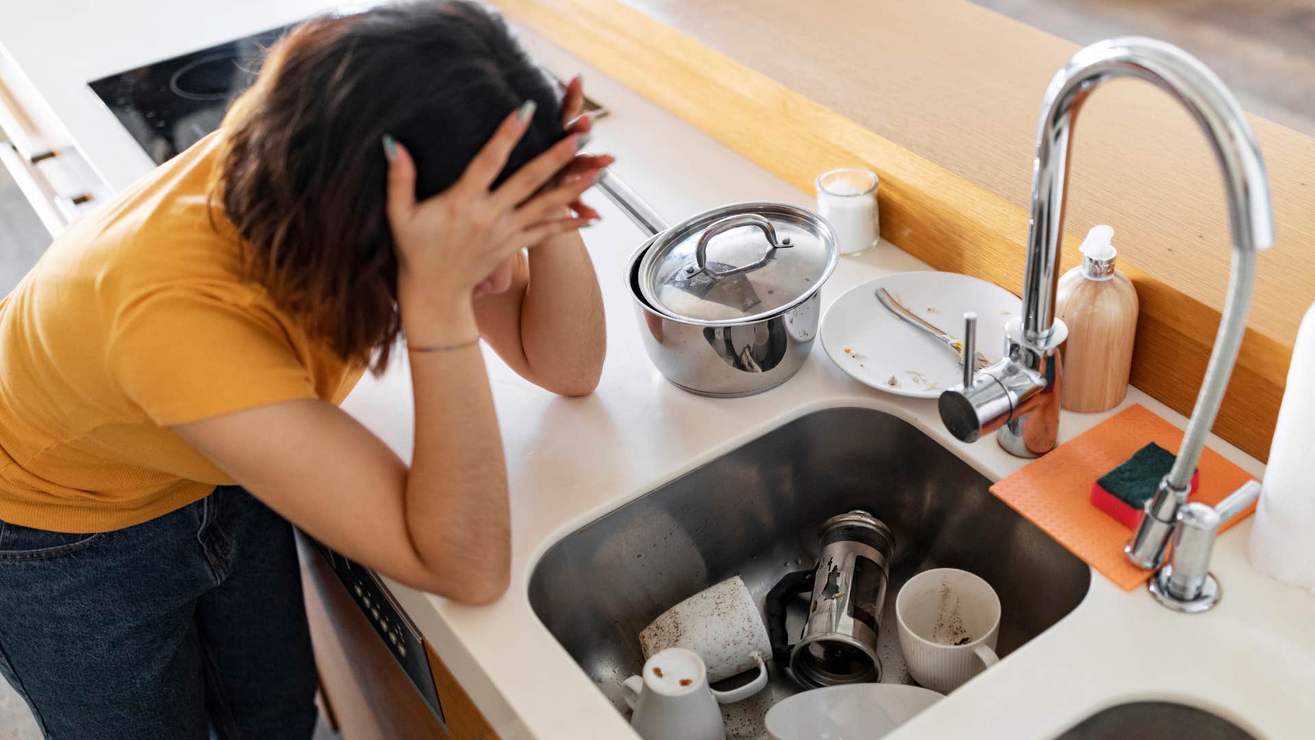 sad woman looking at sink of dirty dishes
