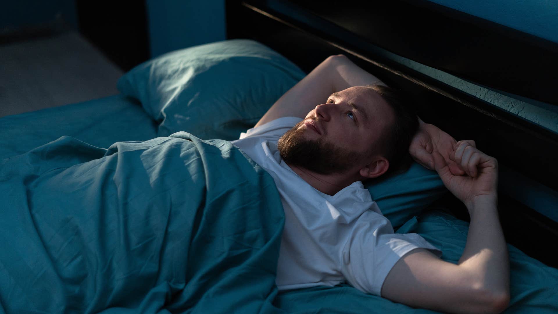 man laying awake in bed feeling anxious