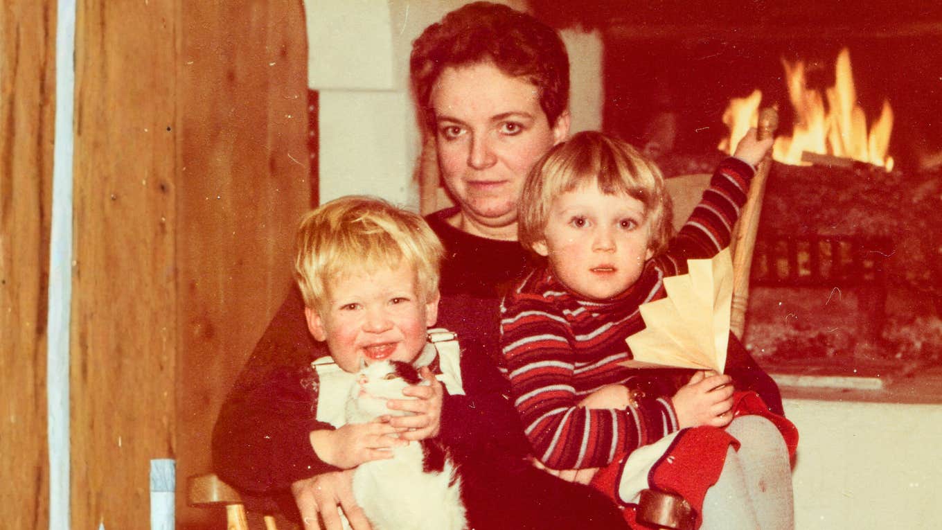 Vintage family photo of a mom and two young children by a fireplace showing the unhinged things someone thought were normal growing up