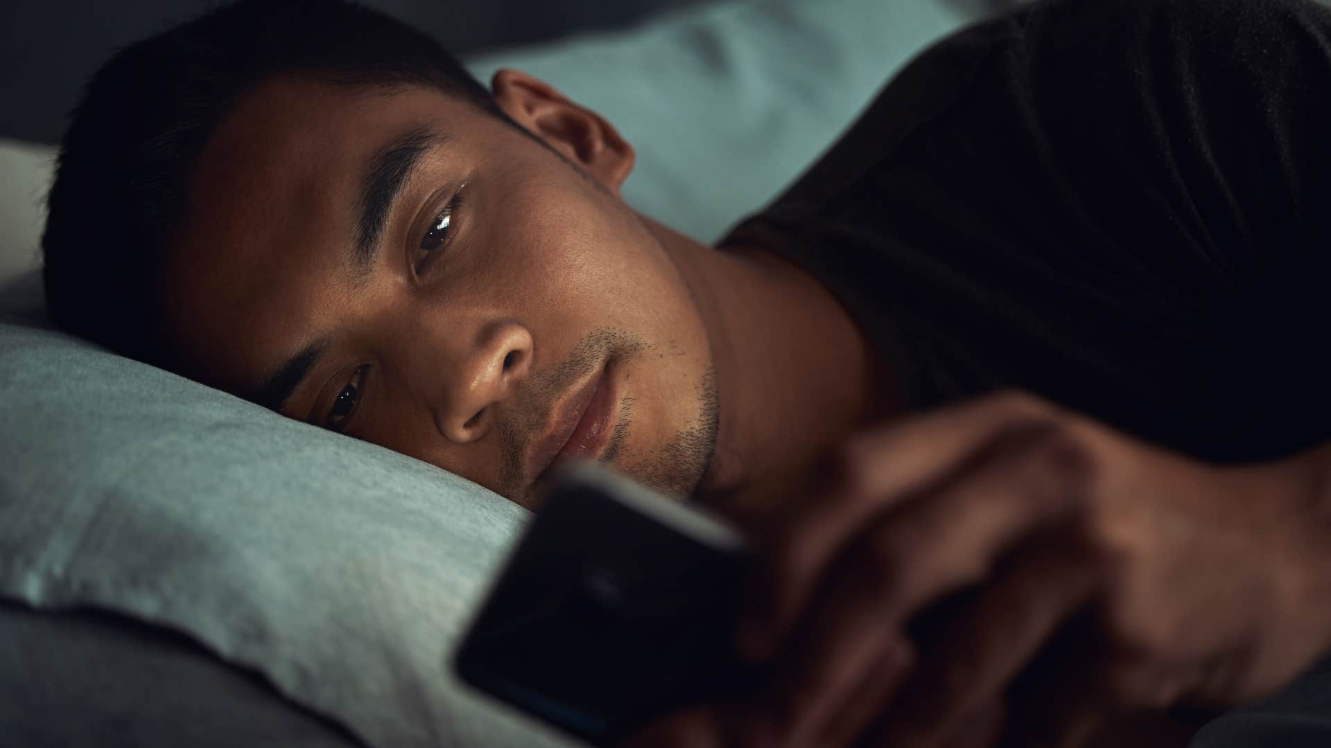unhappy man constantly checking his phone in bed