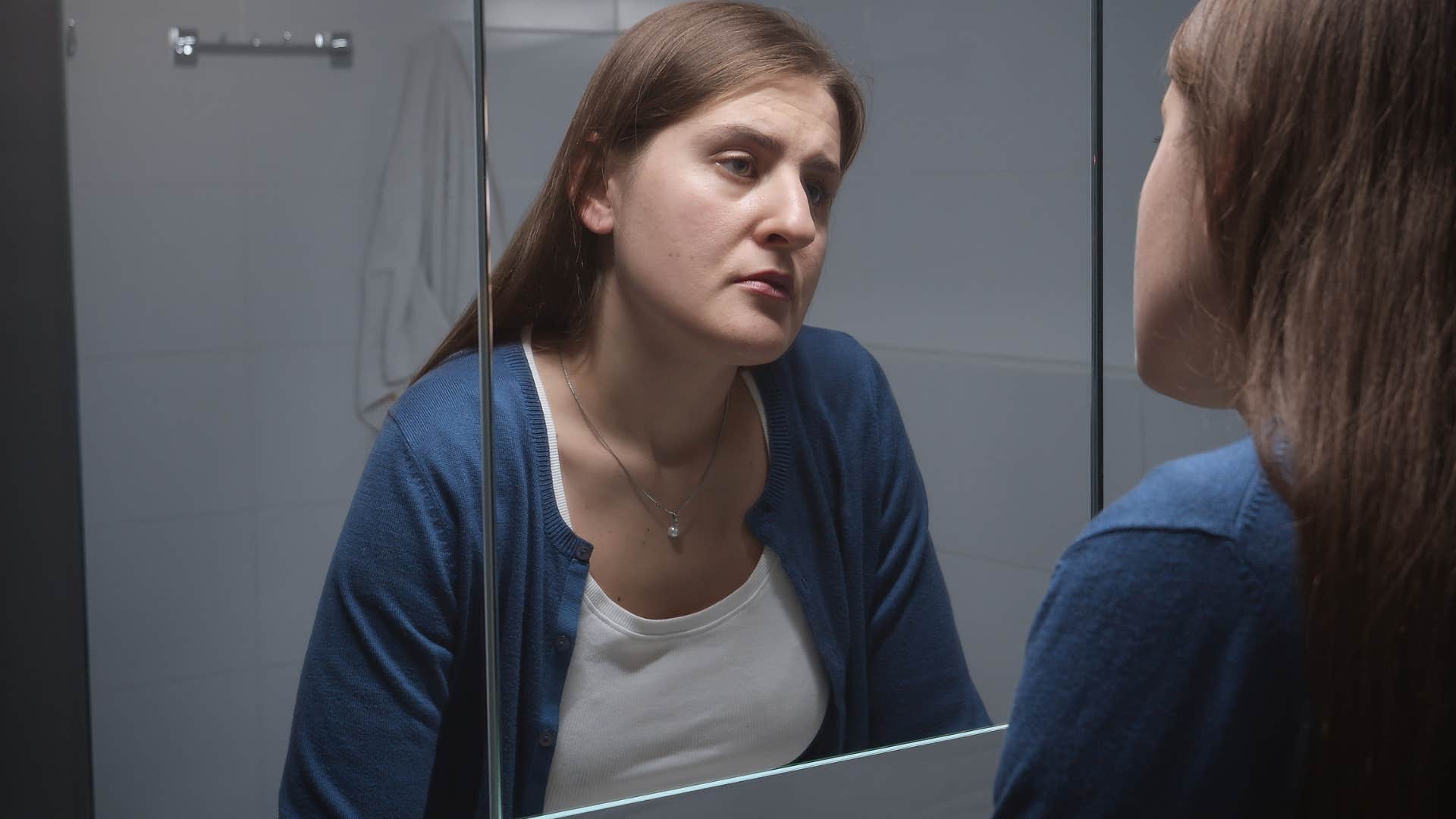woman who criticizes her appearance looking in the mirror