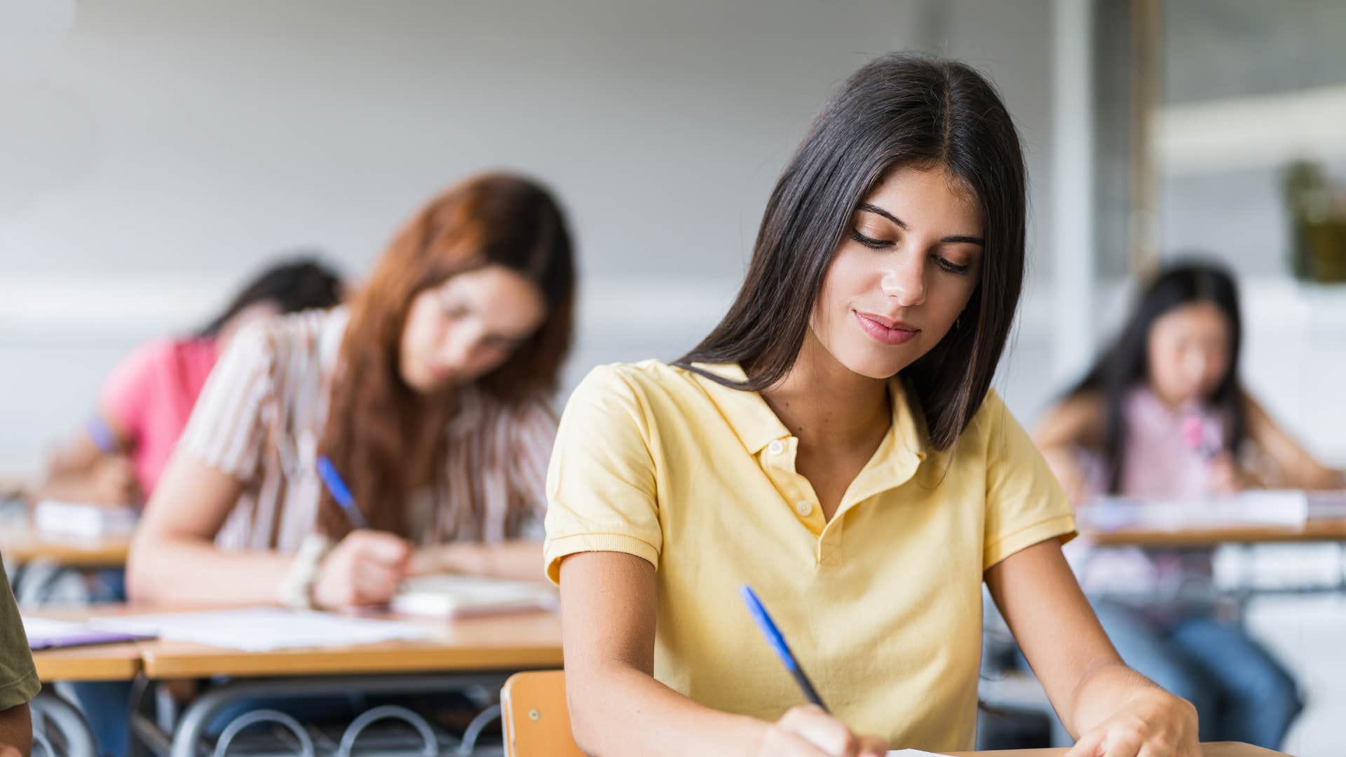 teenager in yellow being taught strength based virtues as she writes notes in class and works hard