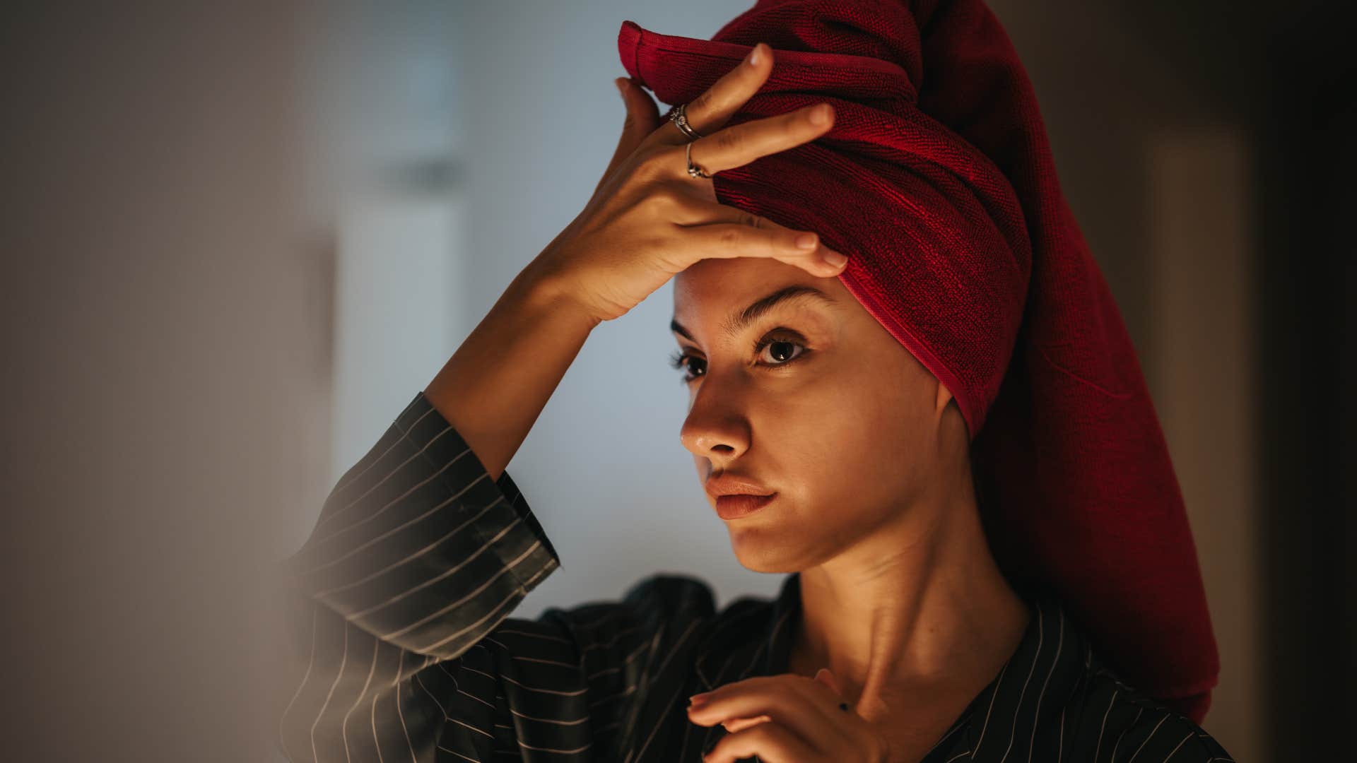 woman with towel wrapped around hair applying skincare products