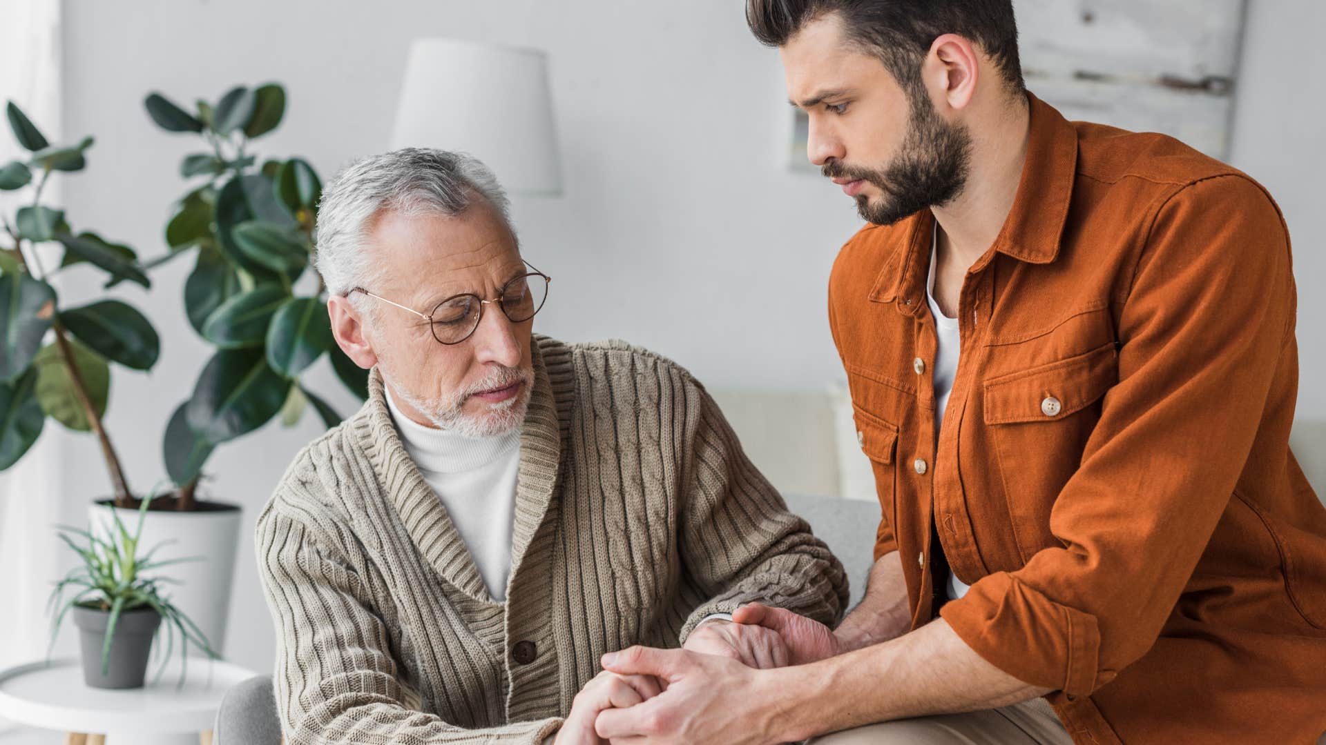 older father holding adult son's hands saying he worries
