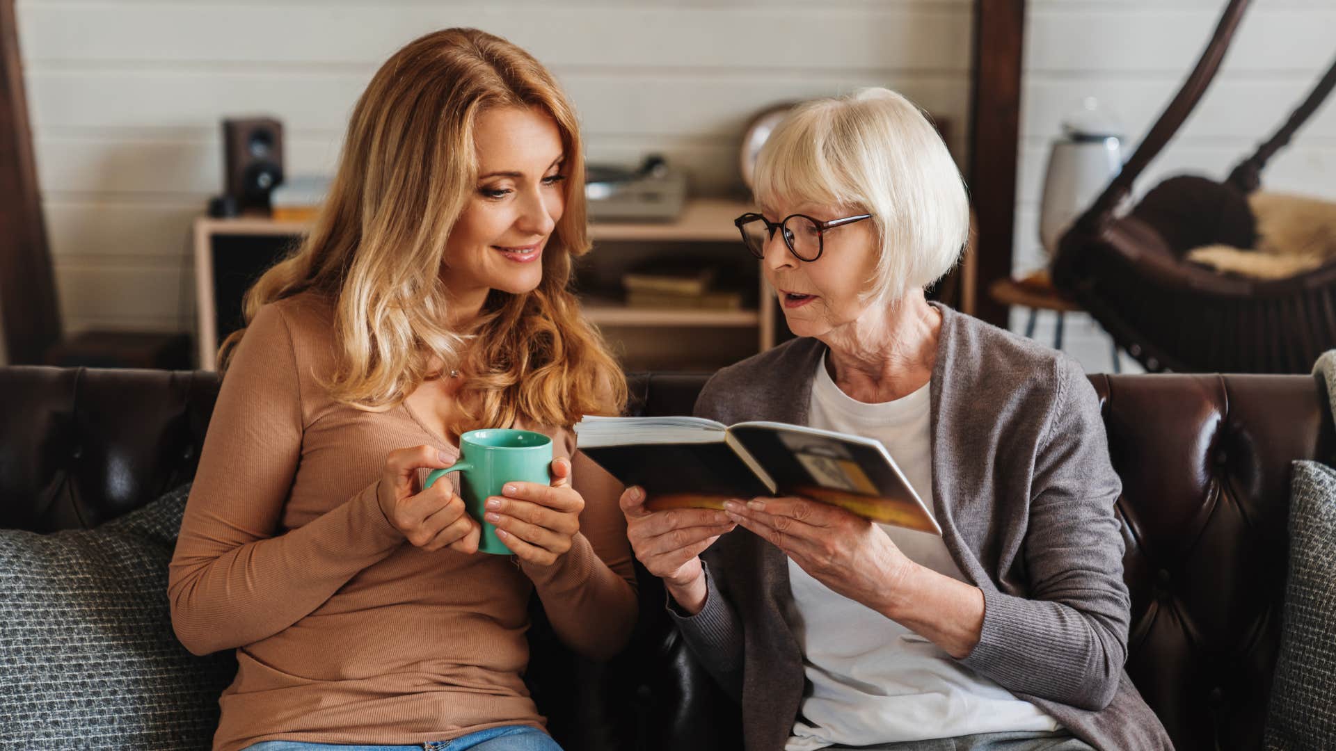 older woman reminiscing with adult daughter reading a book